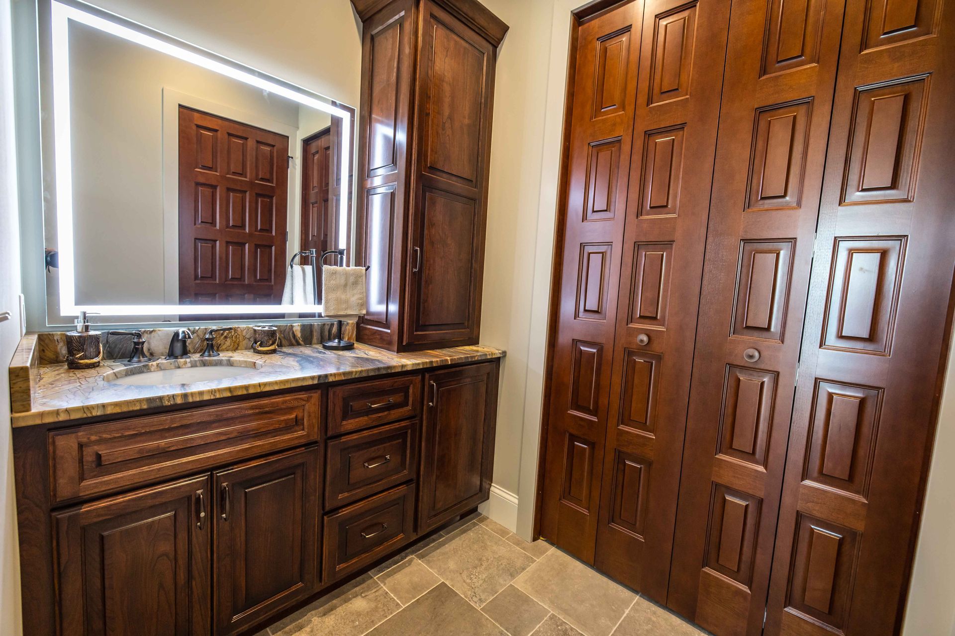 Bathroom with dark wood cabinetry, granite countertop, large mirror, and closet doors.