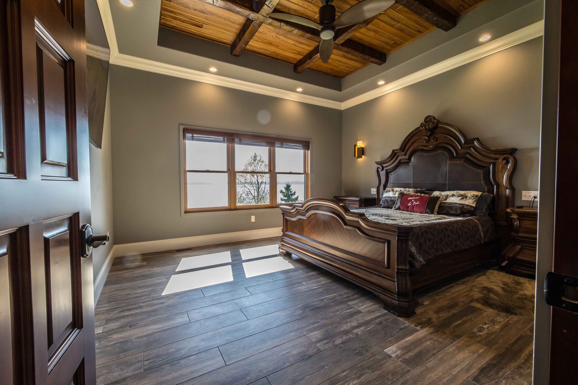 Bedroom with large dark wood bed, gray walls, wood-beam ceiling, and open door.