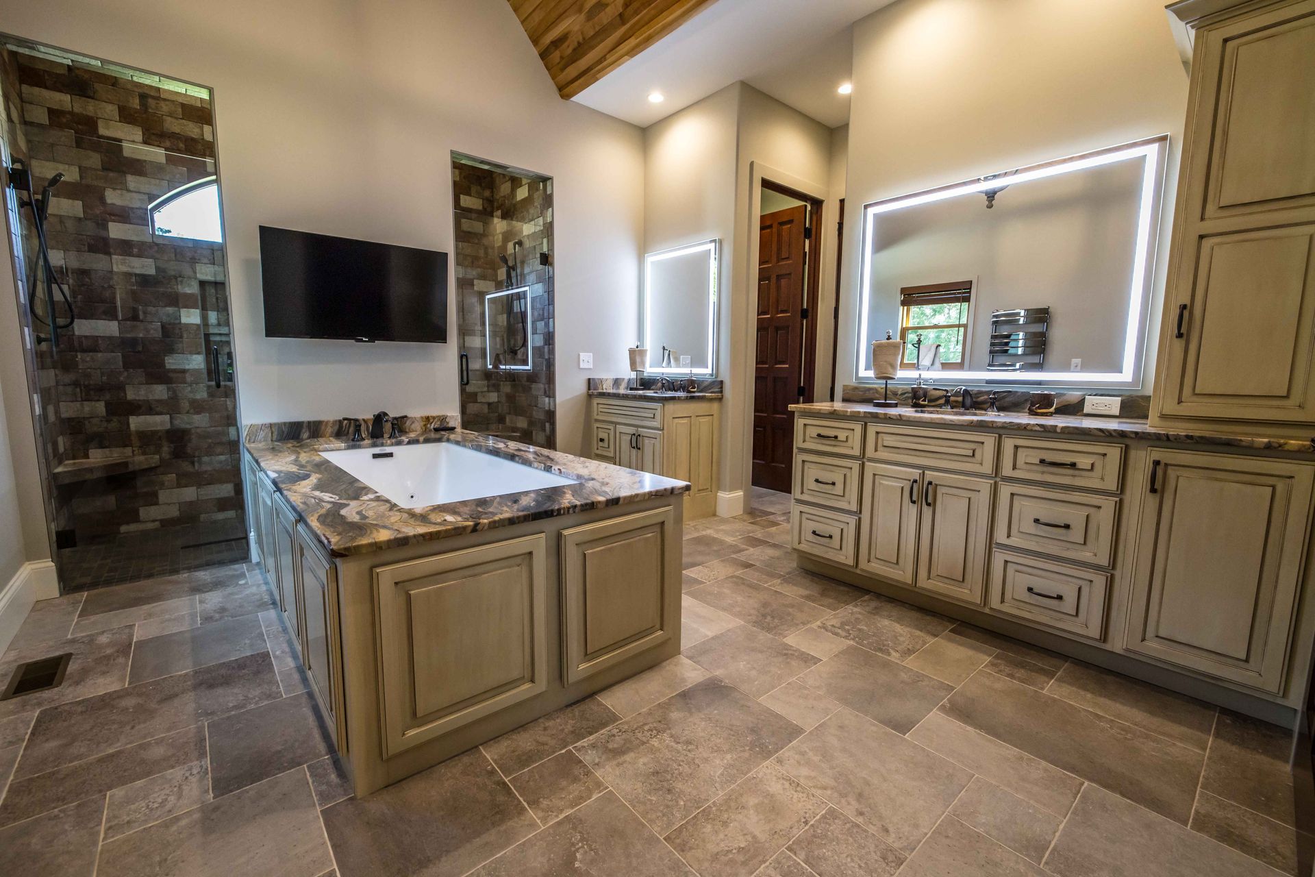 Spacious bathroom with soaking tub, double vanity, and separate shower. Neutral tones with stone floors and cabinetry.