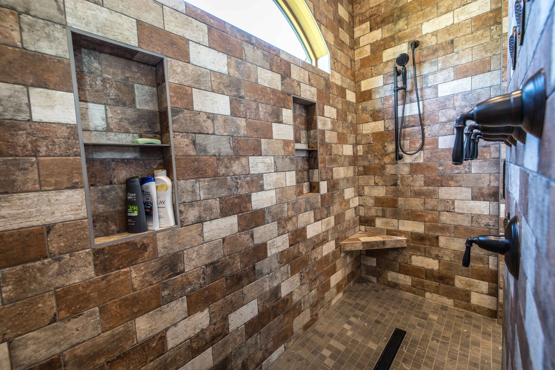 A shower with brick-like tile walls and a built-in bench. Soap and shampoo bottles in a recessed shelf.