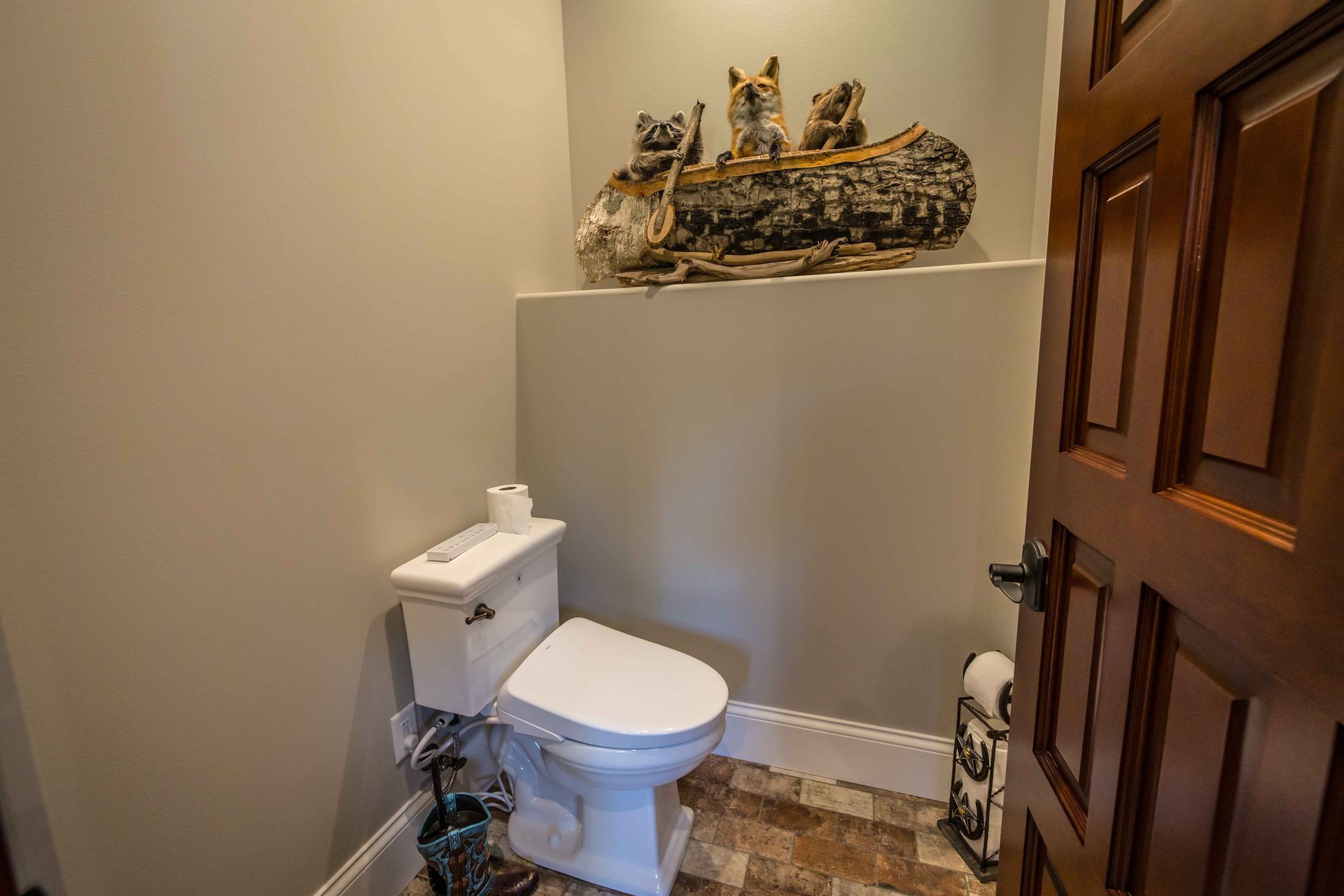 Toilet in a small bathroom with a shelf holding animal figurines, near a dark wood door.