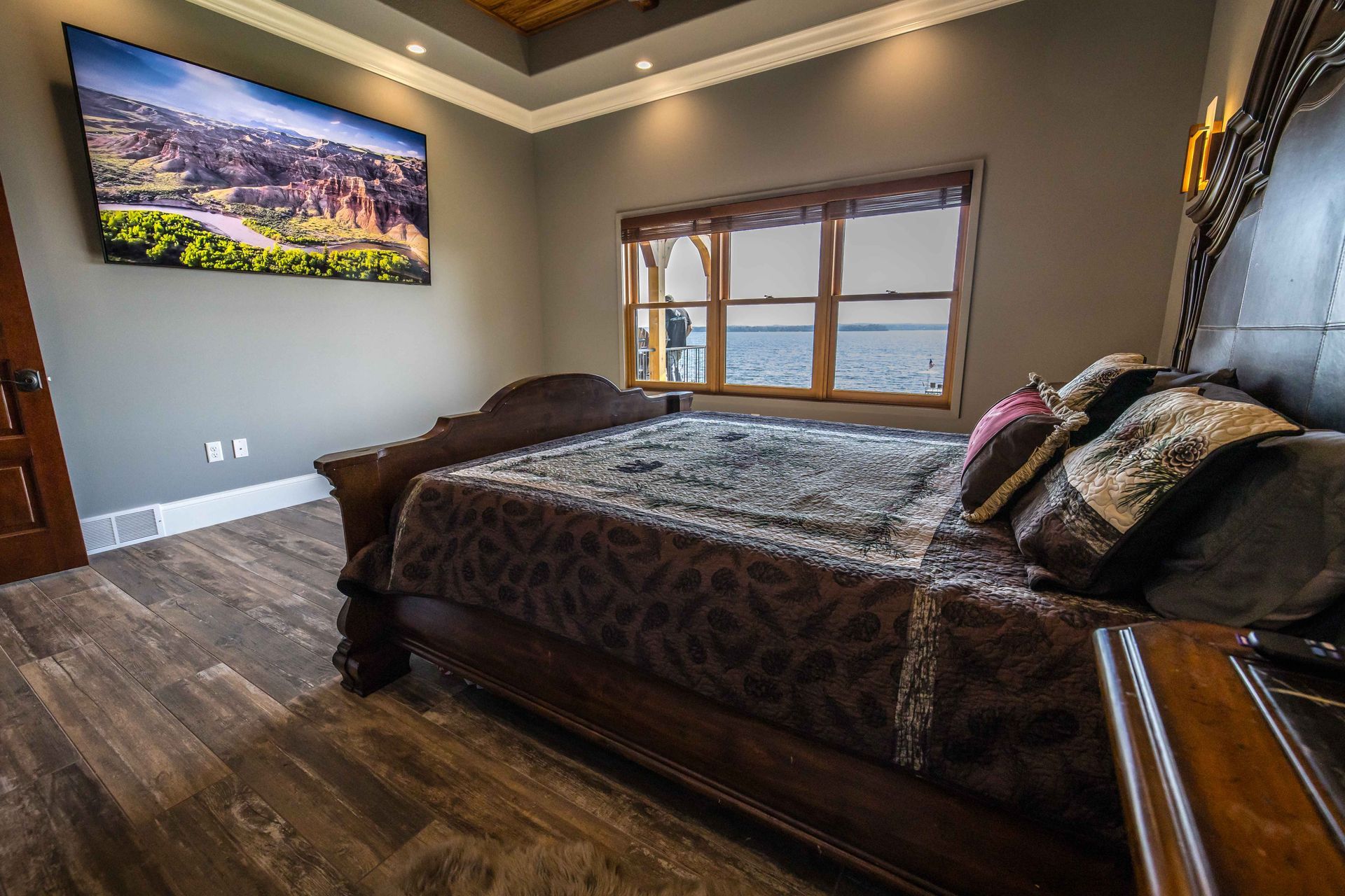 Bedroom with large bed, TV on wall, window with view, and wood flooring.
