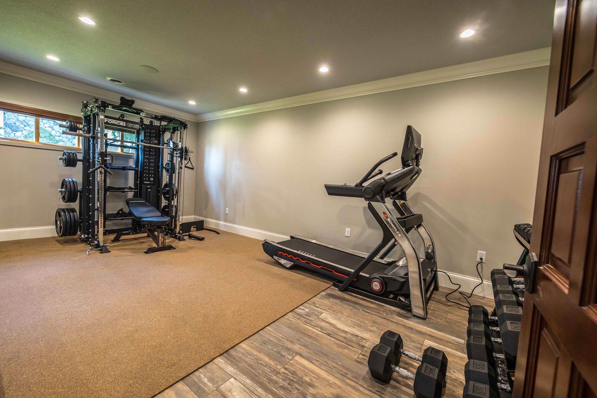 Home gym with weight rack, treadmill, and dumbbells on a neutral-colored floor with grey walls.