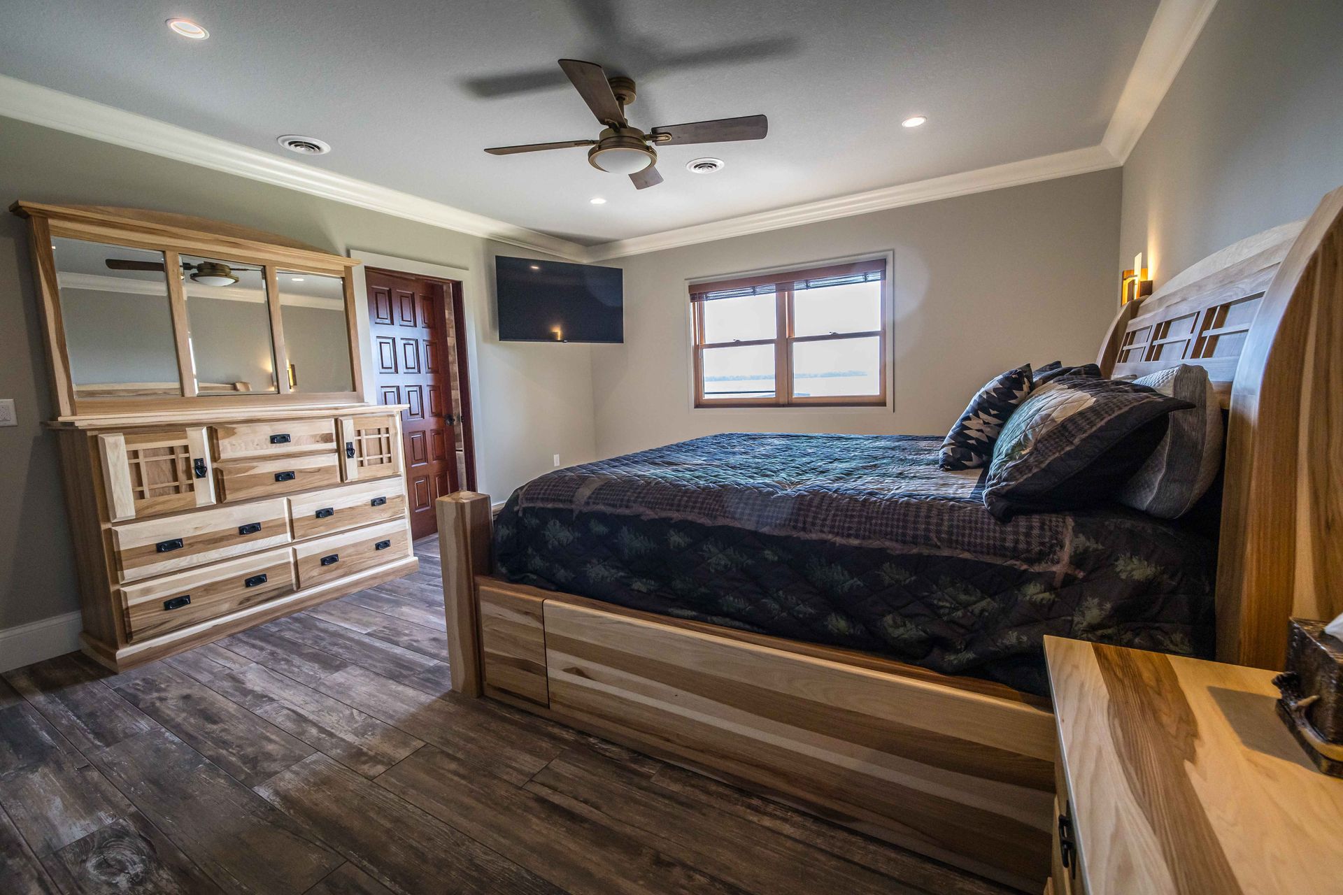 Bedroom with wooden furniture, including a bed, dresser, and nightstand. The walls are gray, and the floor is wood.