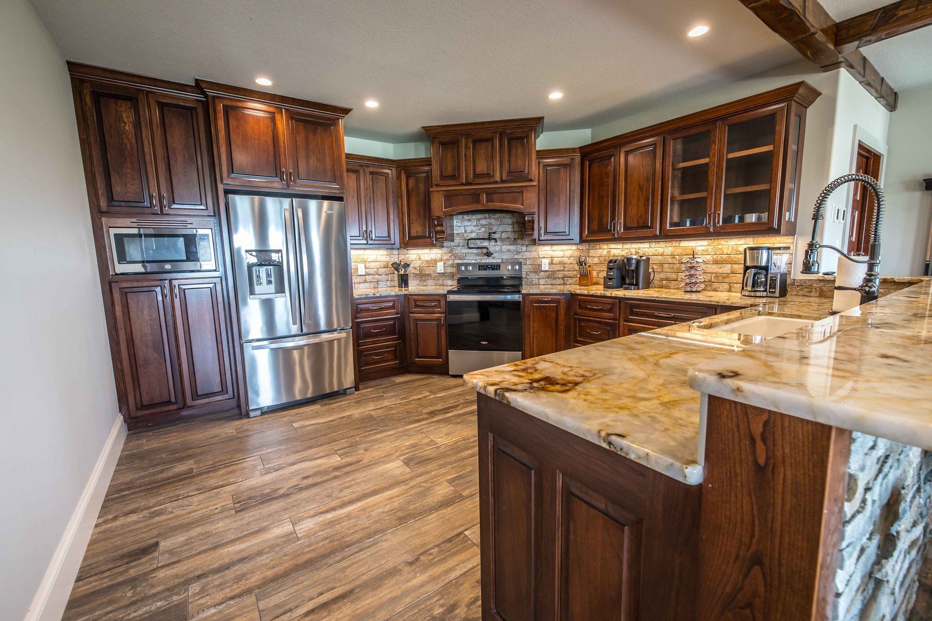 Kitchen with dark wood cabinets, stainless steel appliances, granite countertops, and wood-look tile flooring.