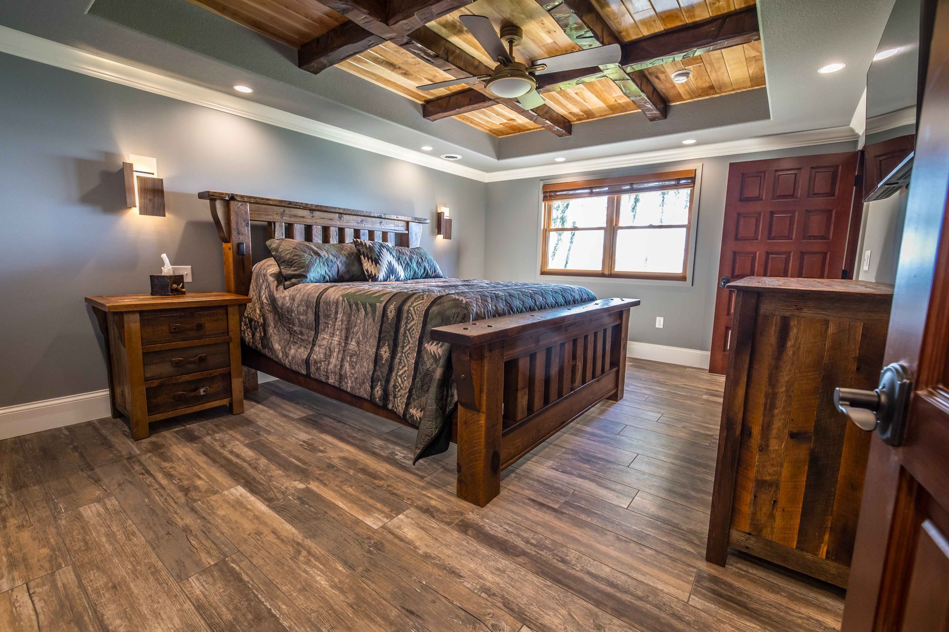 Rustic bedroom with wooden bed, nightstand, and dresser; wood ceiling and flooring, gray walls.