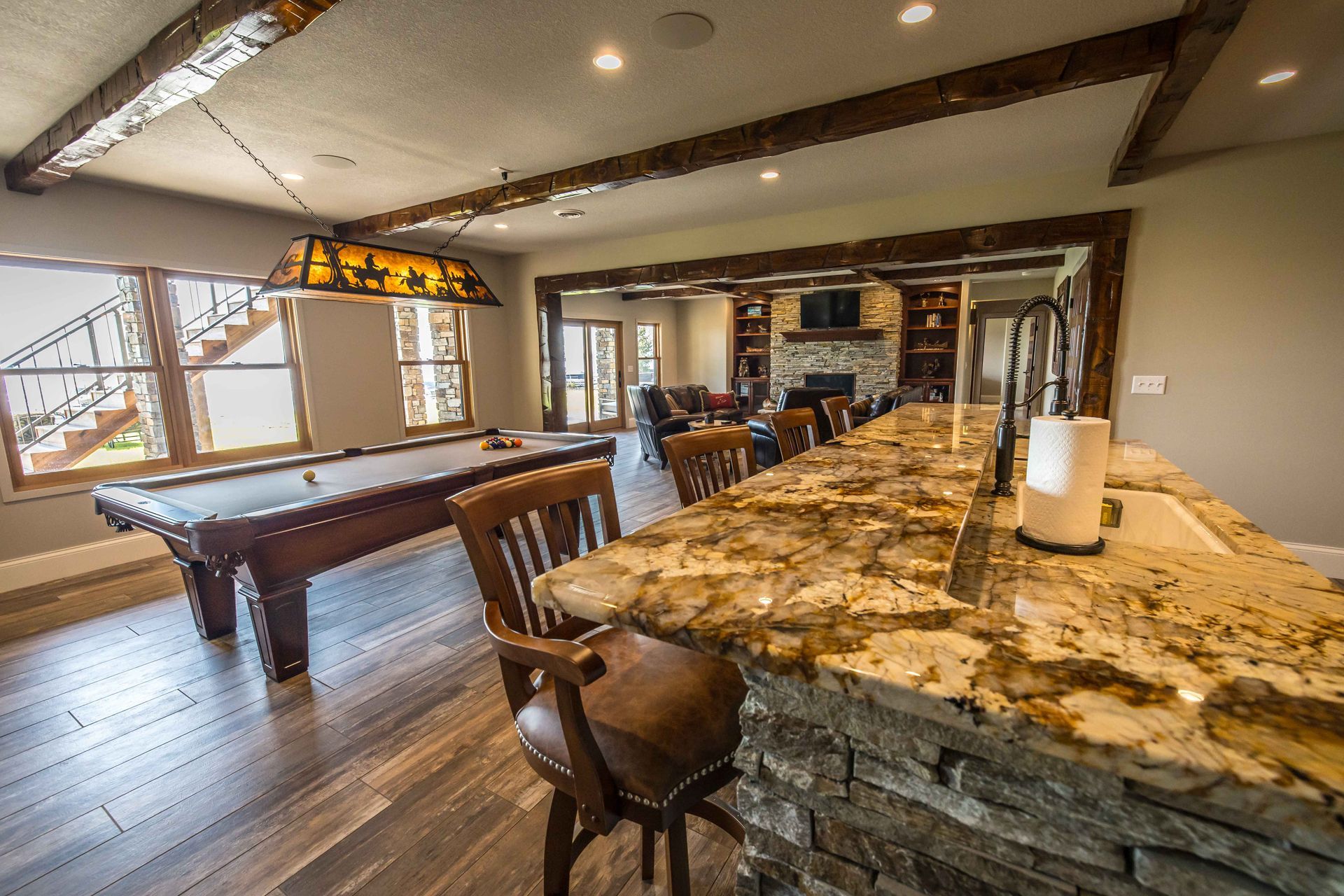 Game room with pool table, bar, and fireplace. Exposed beams, granite countertop, wooden floors.
