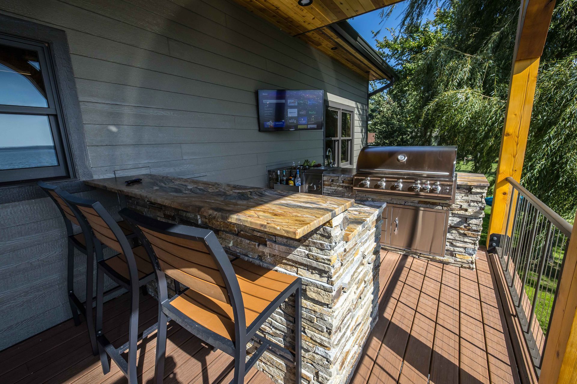 Outdoor kitchen with a granite bar, grill, and TV on a deck.