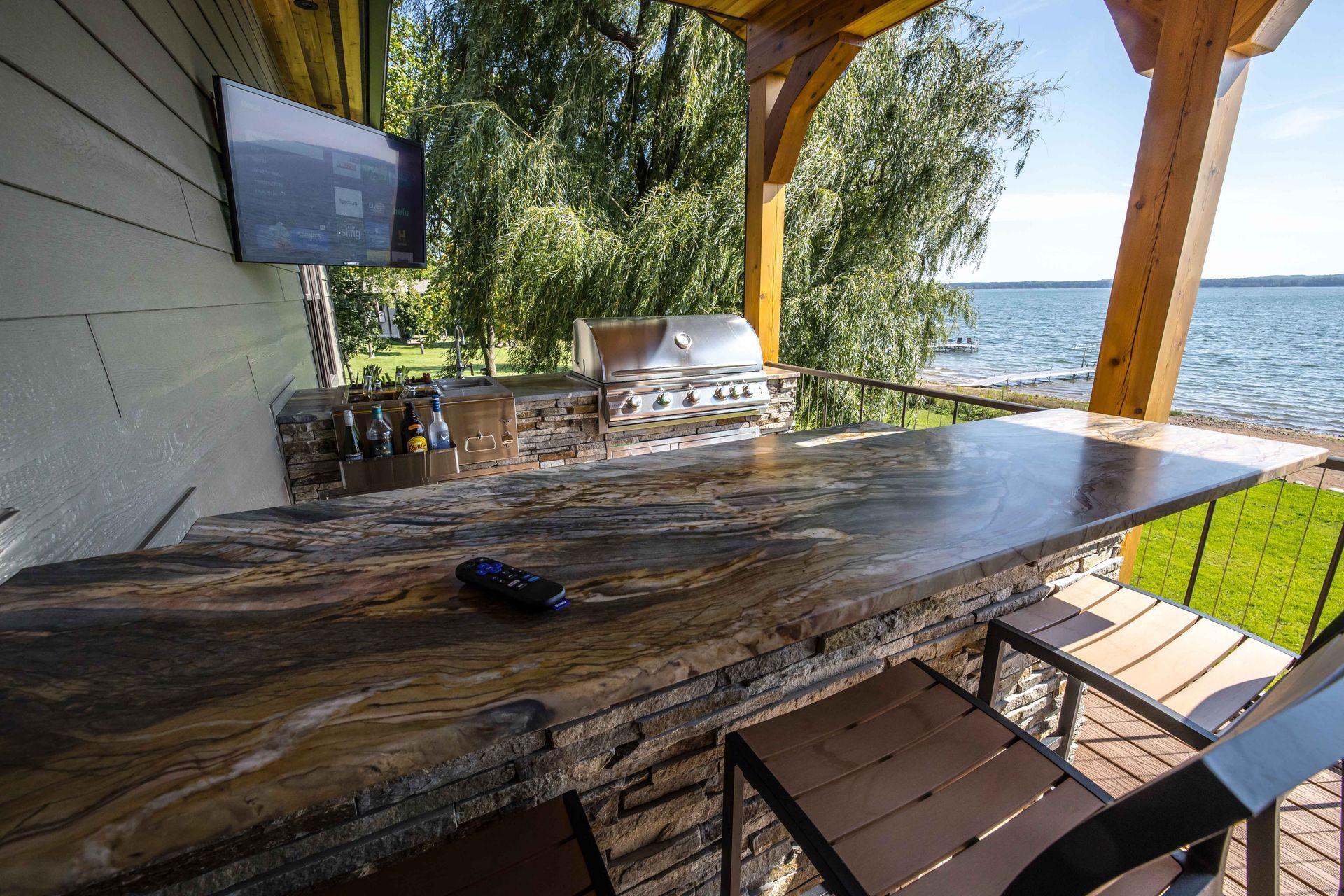 Outdoor kitchen with grill, countertop, TV, and lake view.