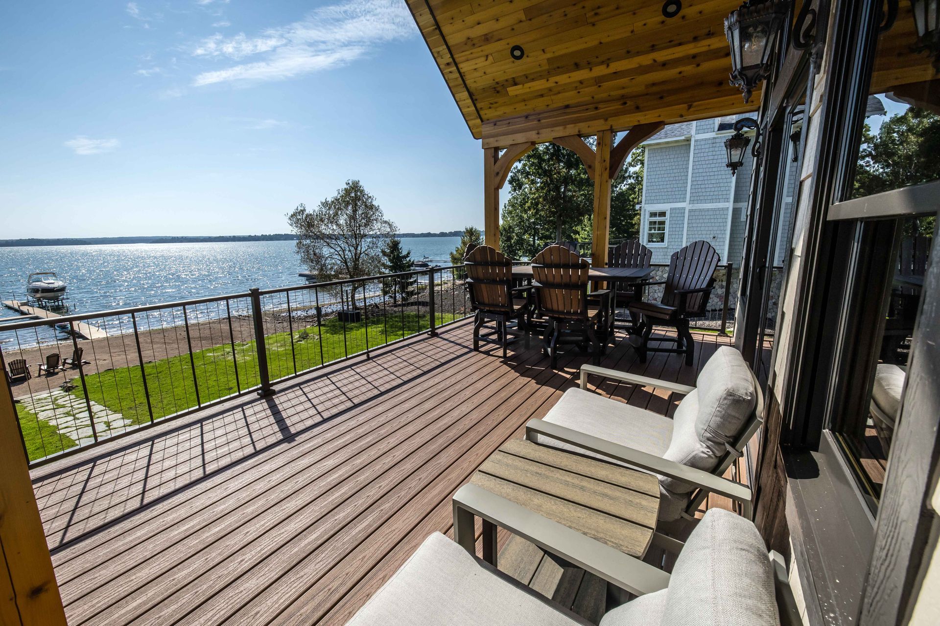 Deck overlooking a lake. Wooden deck with chairs, table, and railing. Sunny day, blue water.