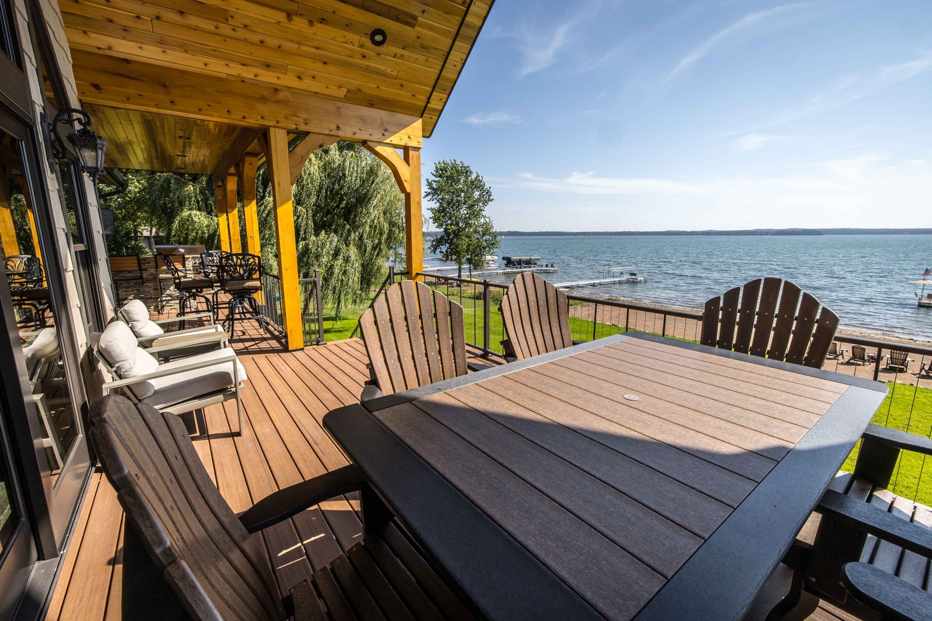 Wooden deck with lake view, Adirondack chairs around a table, under a wooden ceiling.