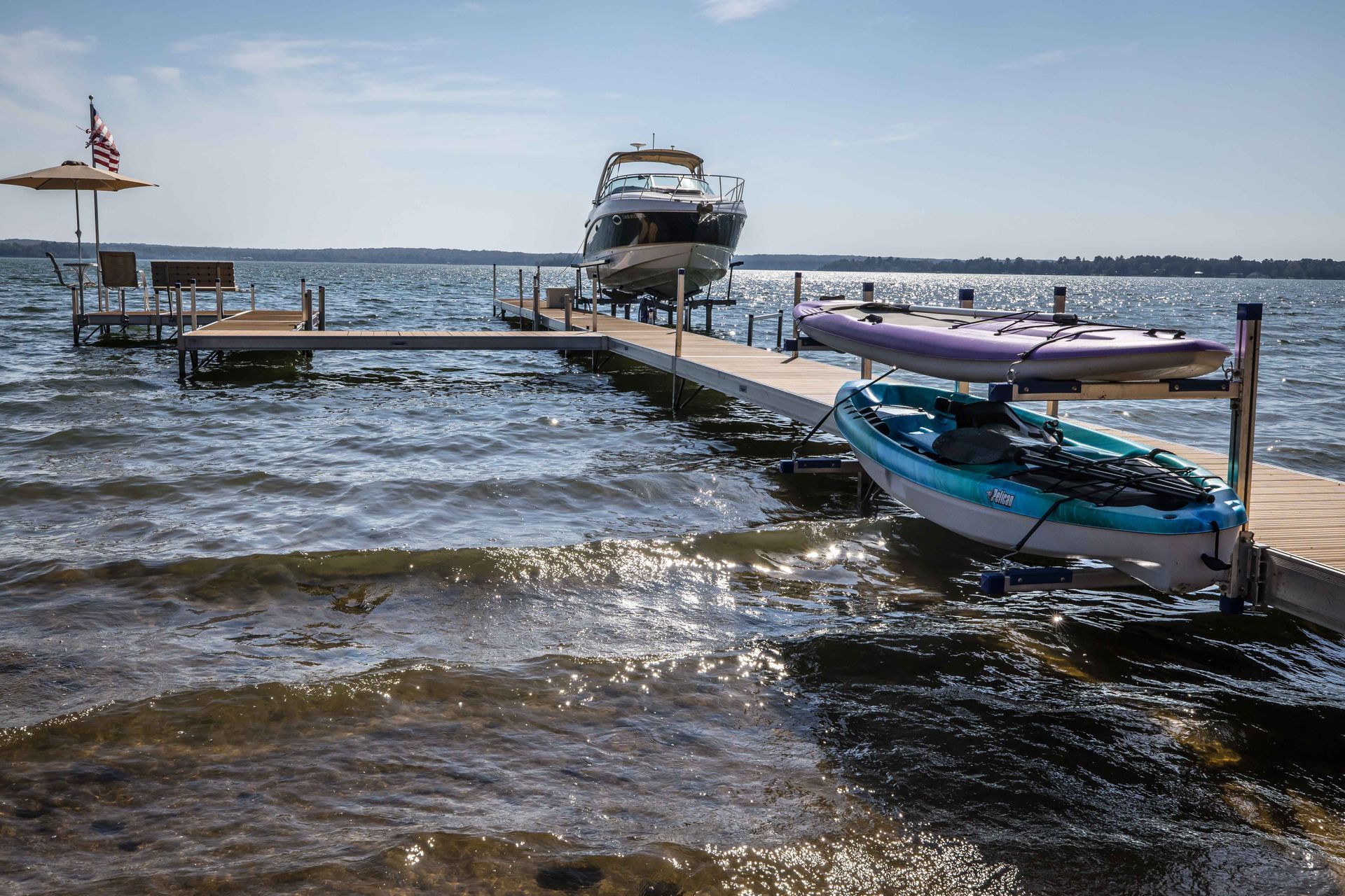 Dock on a lake with a boat, kayaks, and an American flag on a sunny day.