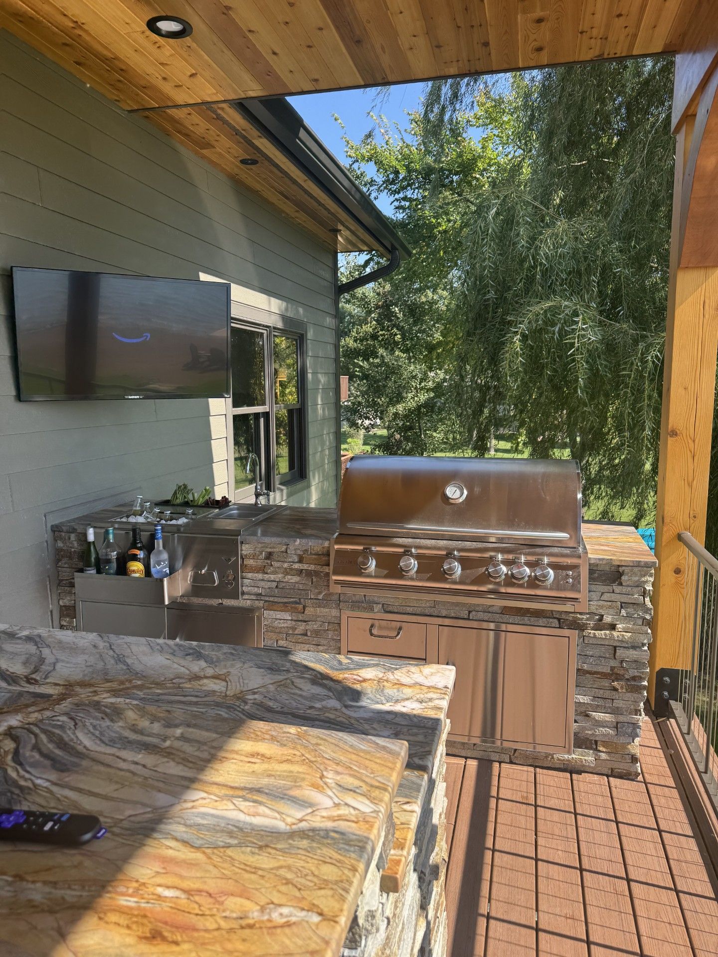 Outdoor kitchen with stainless steel grill, granite countertop, and mounted TV.