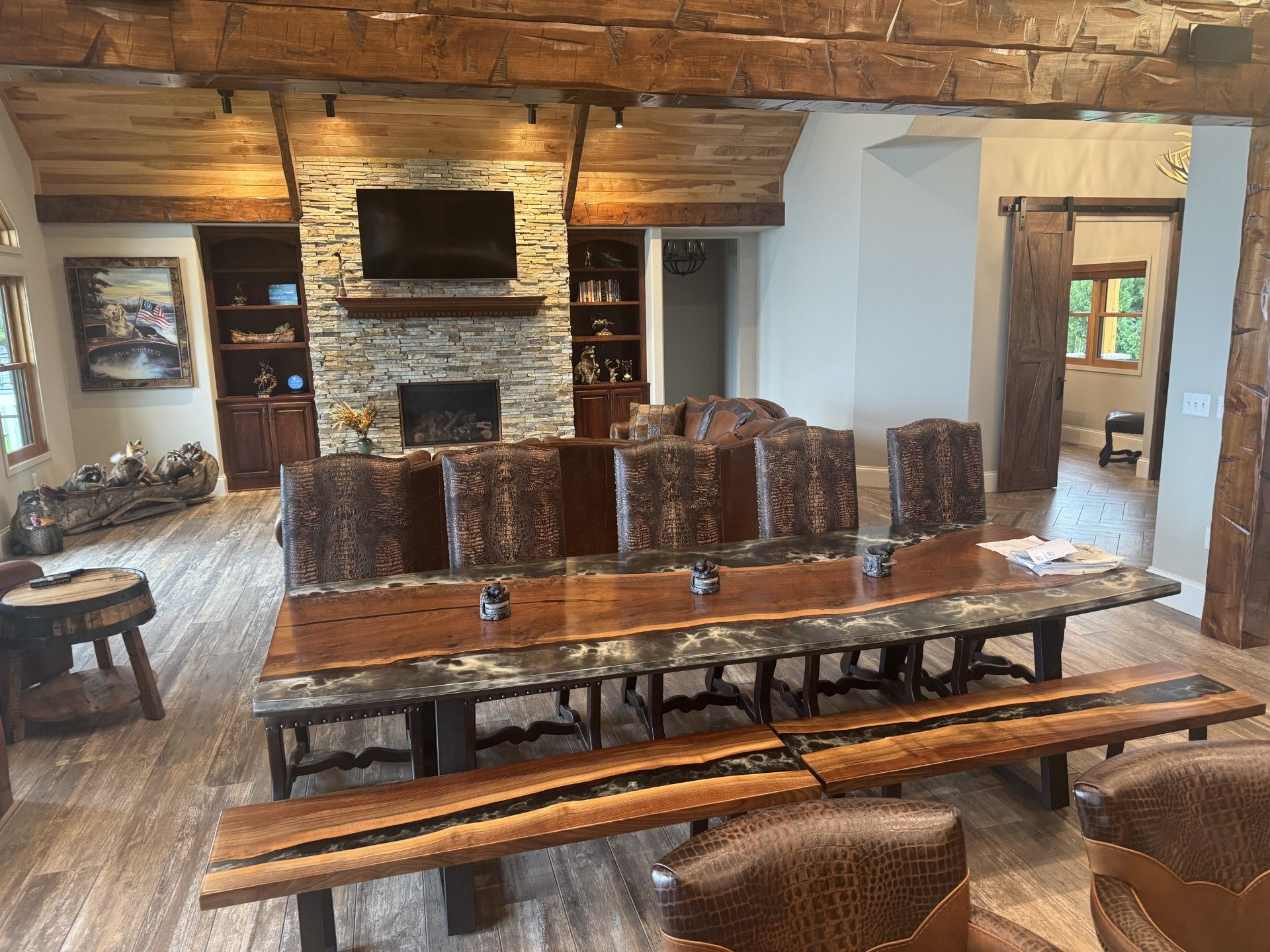 Rustic dining room with a long wood table, leather chairs, fireplace, and exposed beams.