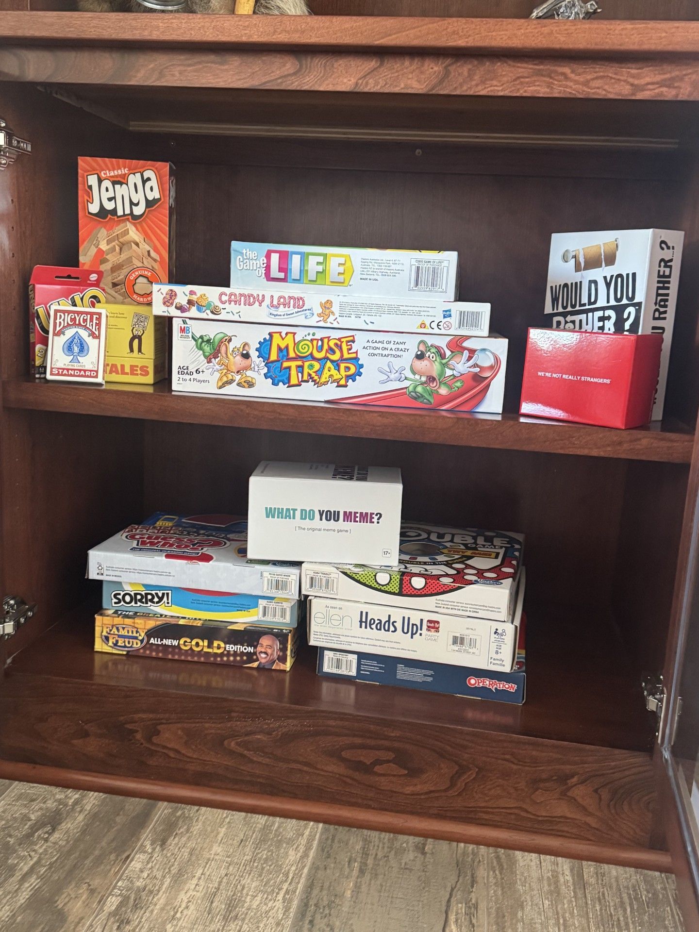 Wooden cabinet with board games on shelves: Jenga, Life, Trouble, decks of cards, and more.
