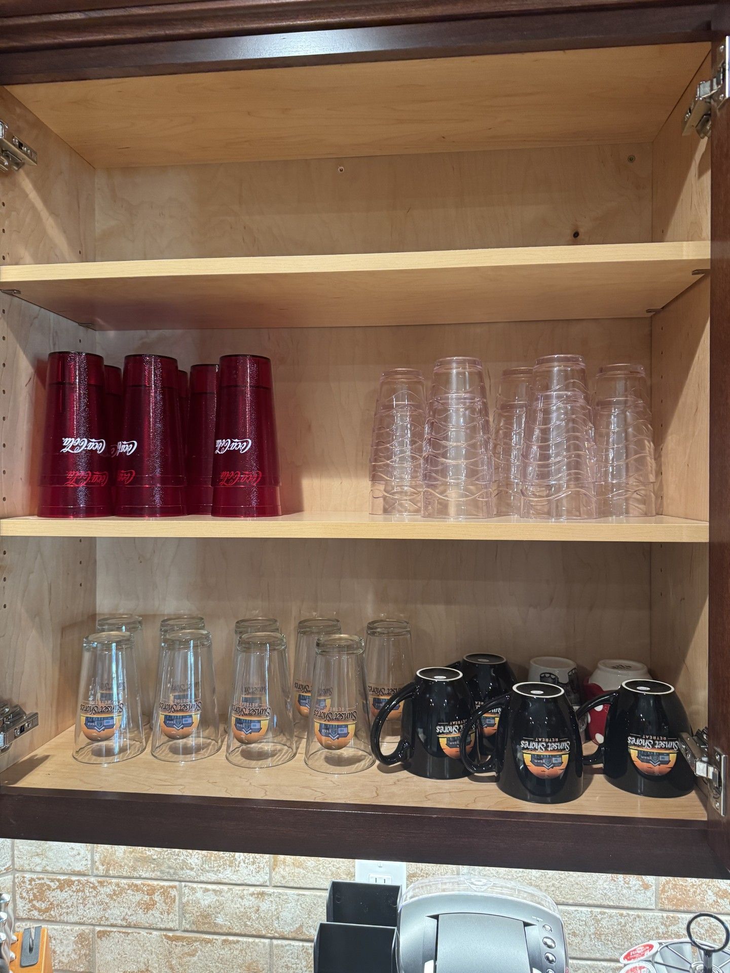 Cabinet with shelves holding stacks of red and clear cups, plus some mugs and glass tumblers.