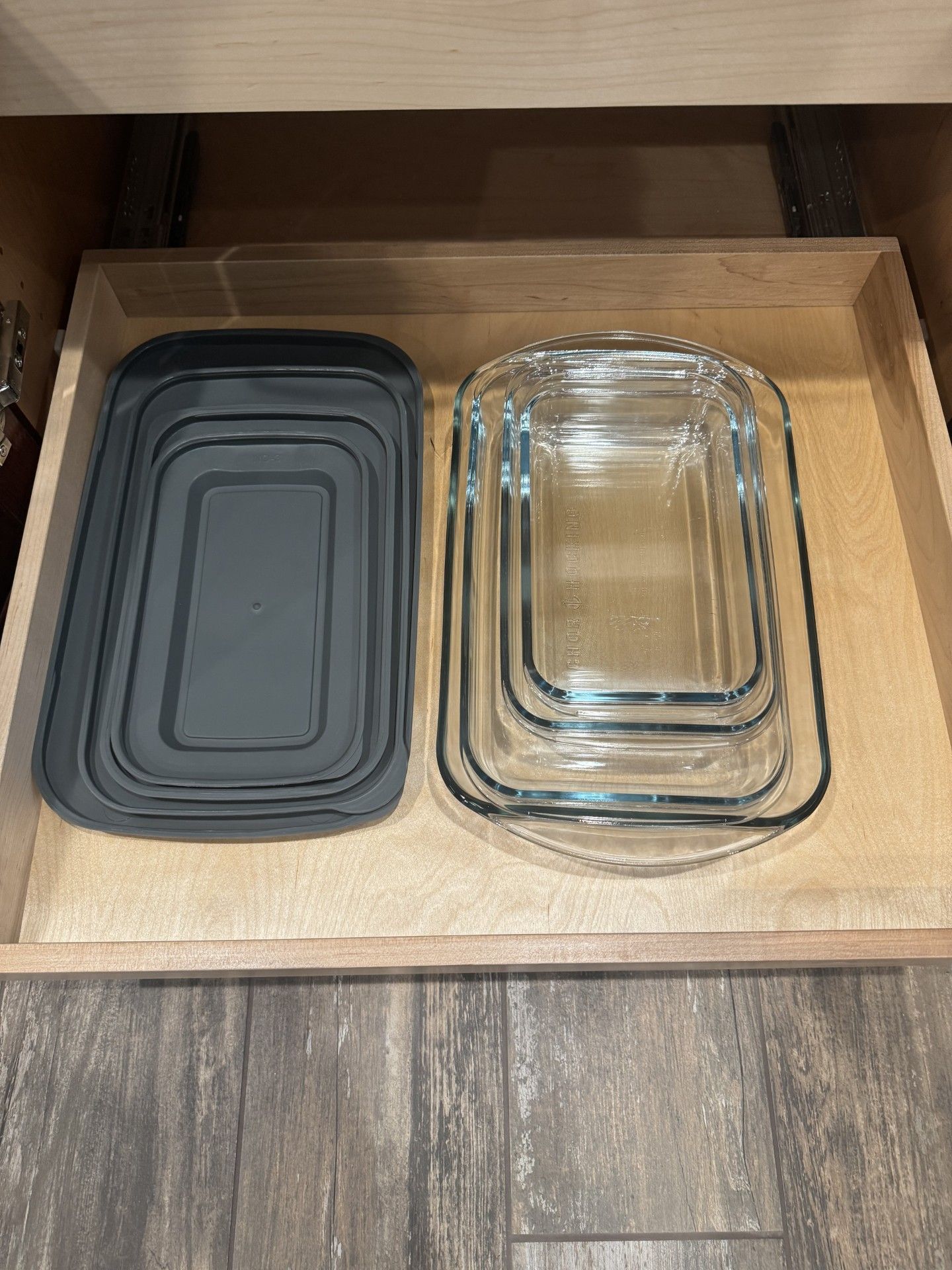 A kitchen drawer with baking dishes. Stacked gray plastic and clear glass rectangular pans. Wooden drawer interior.