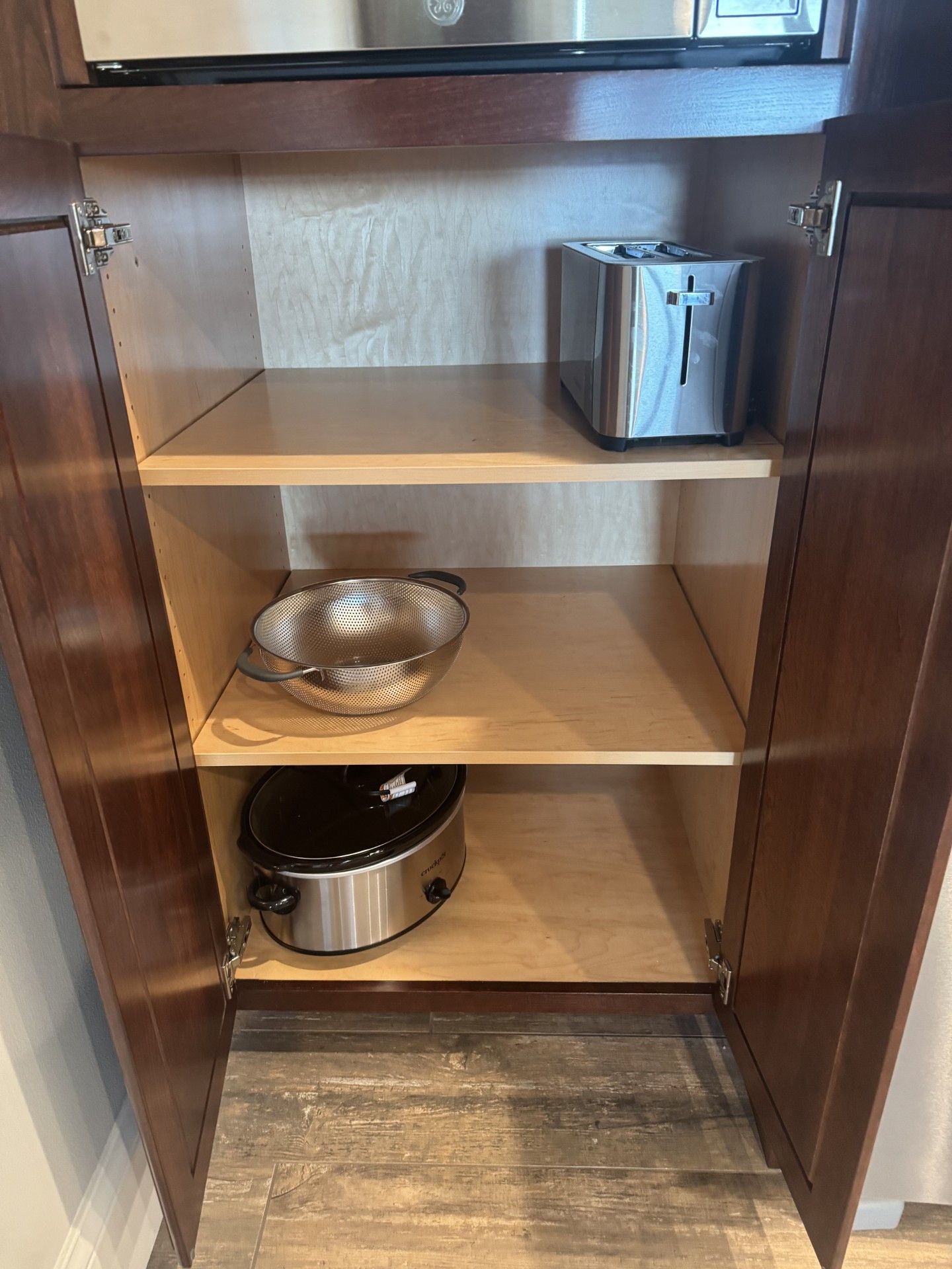 Open cabinet with a toaster, food processor, and slow cooker on shelves.