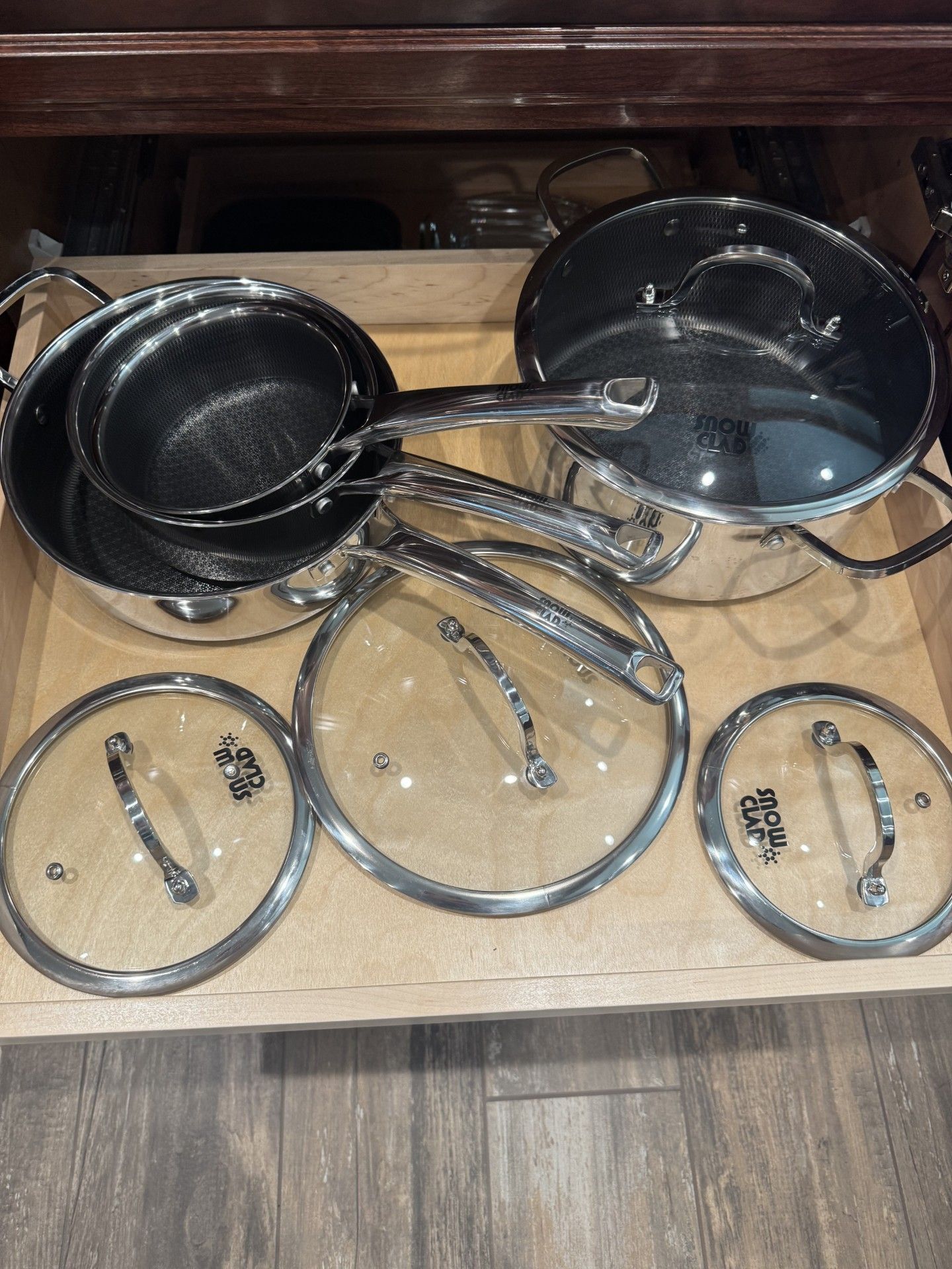 Pots and pans with glass lids inside an open kitchen drawer.