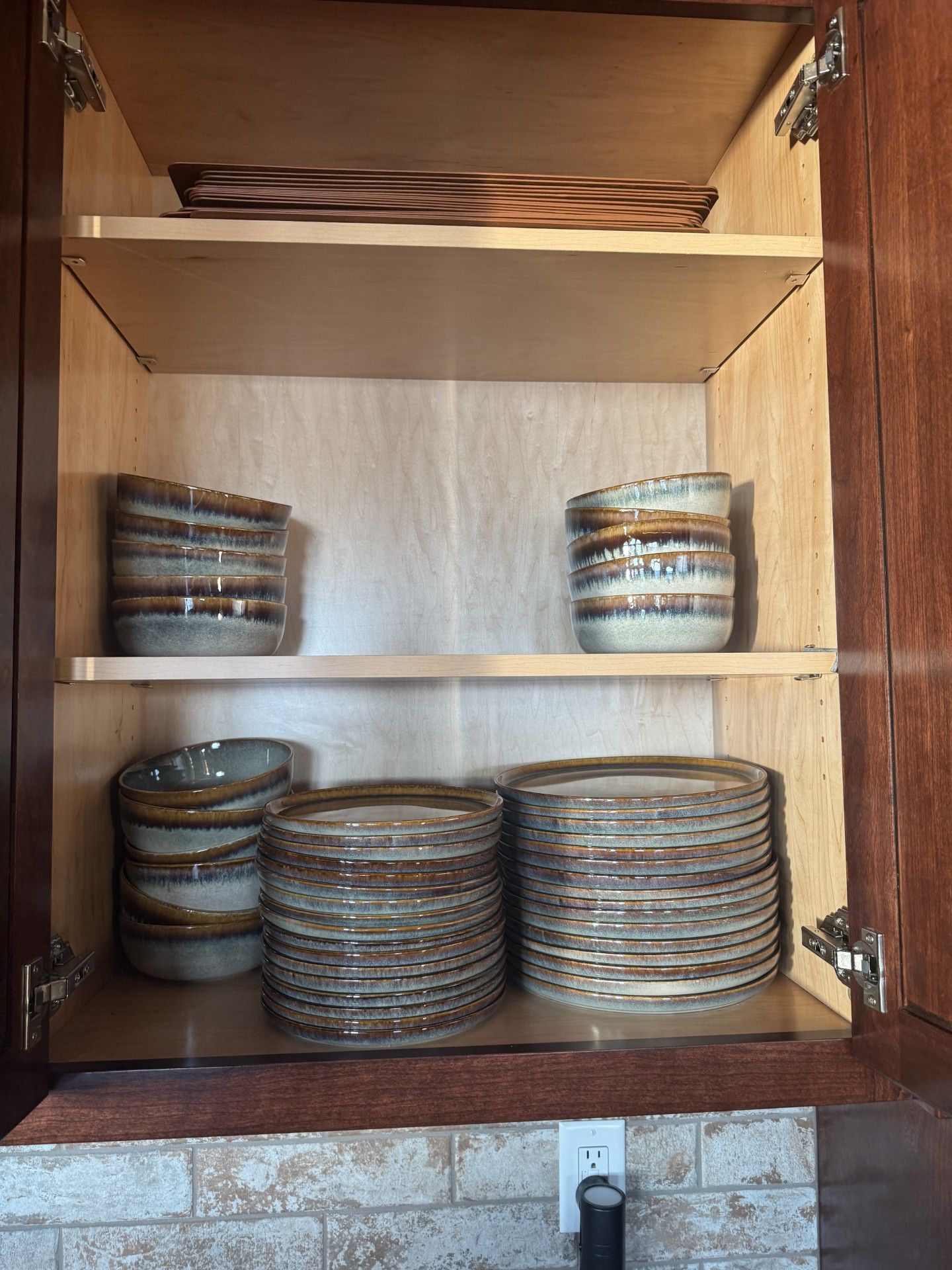 Cabinet with stacked brown and beige dishes and bowls on shelves.