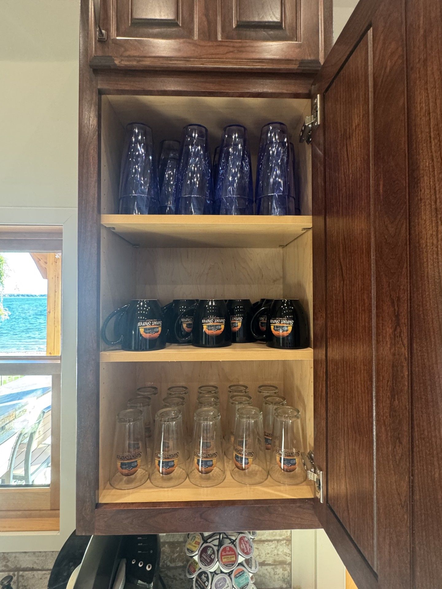 A cabinet with shelves holding blue glasses, black mugs, and clear stemware.
