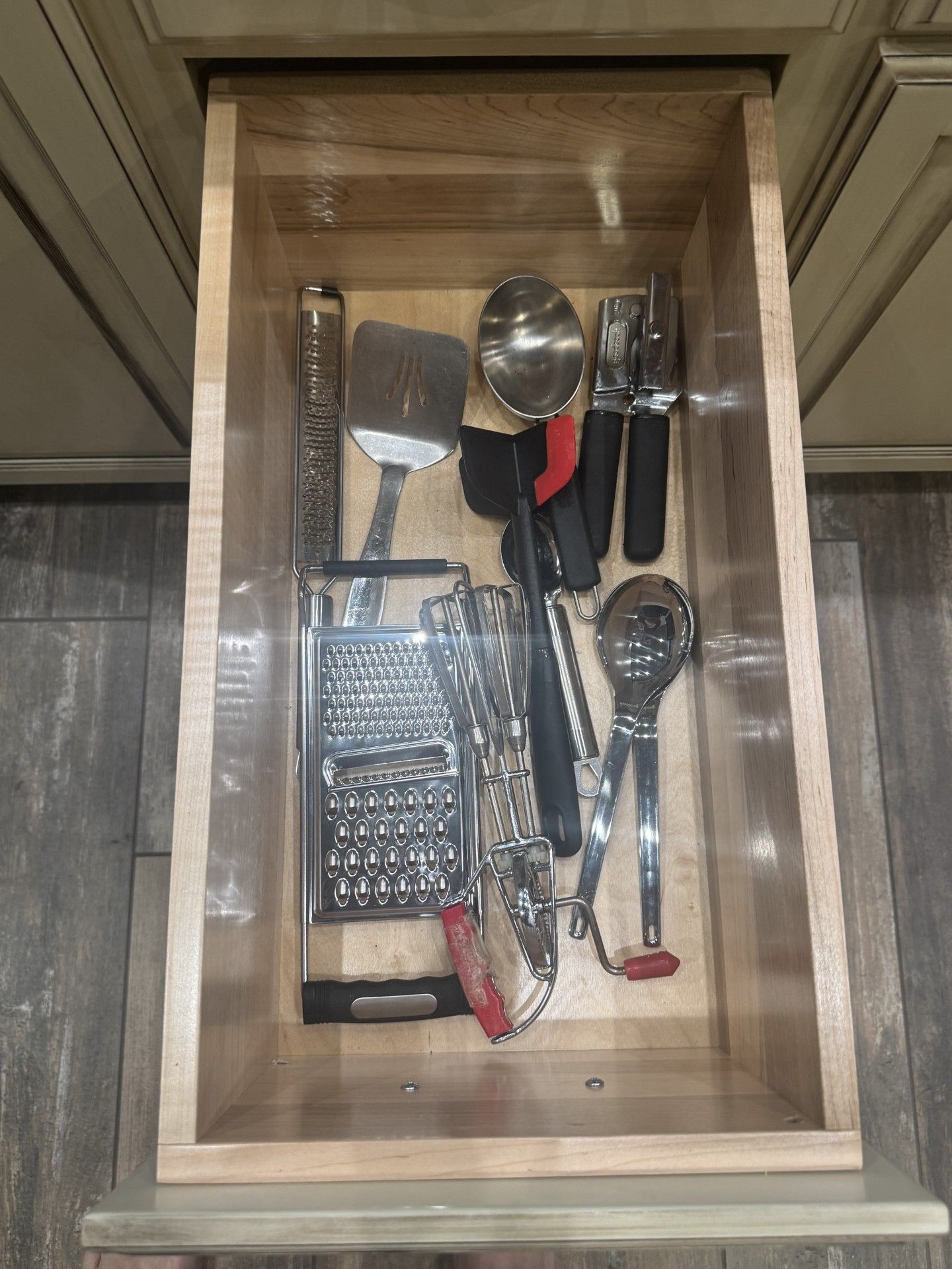 A drawer filled with kitchen utensils: spatula, grater, spoon, can opener, and other tools.