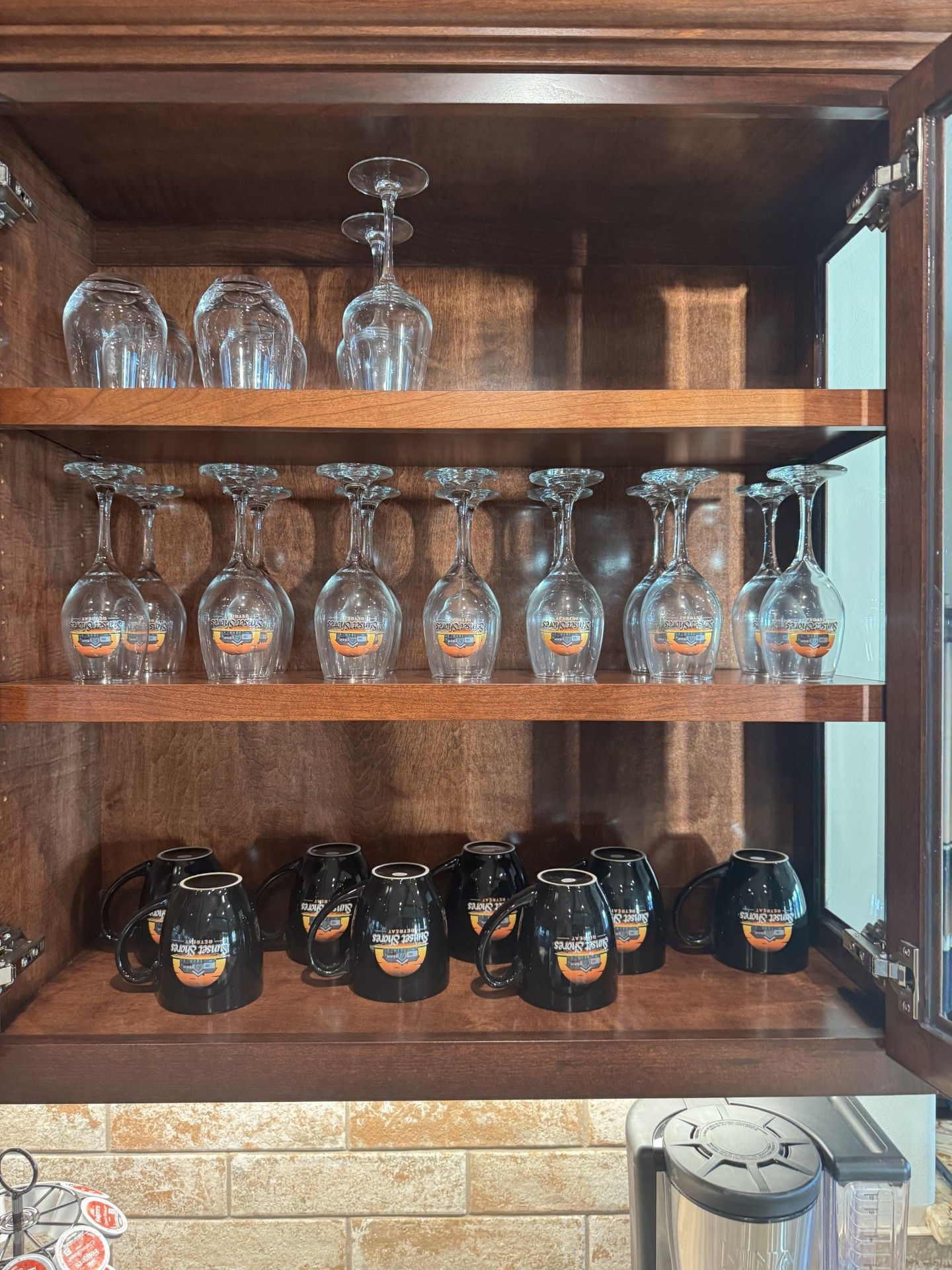 Wooden cabinet with shelves holding upside-down wine glasses and mugs; a kitchen setting.
