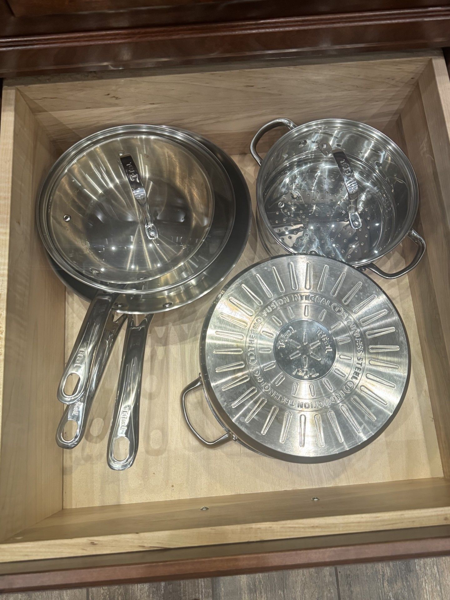 Silver pots and pans in an open wooden drawer.