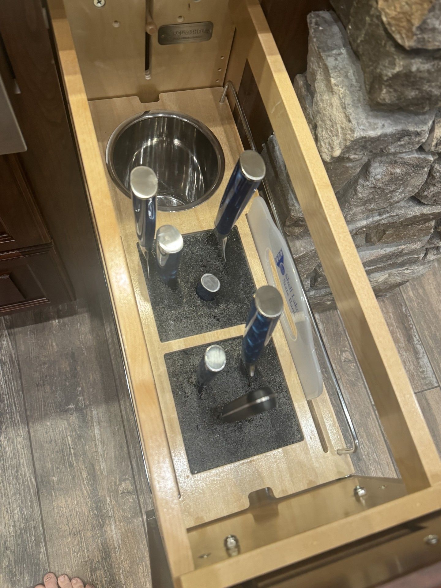 Open kitchen drawer with knife storage and a bowl. Drawer has wood frame.