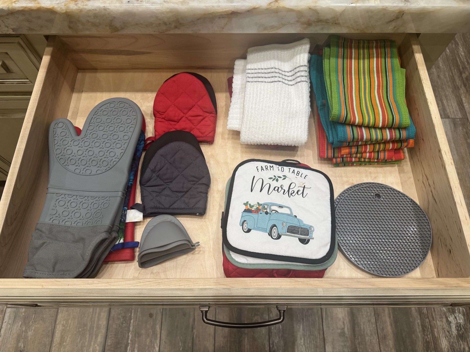 A drawer holding oven mitts, pot holders, and kitchen towels in various colors and designs.