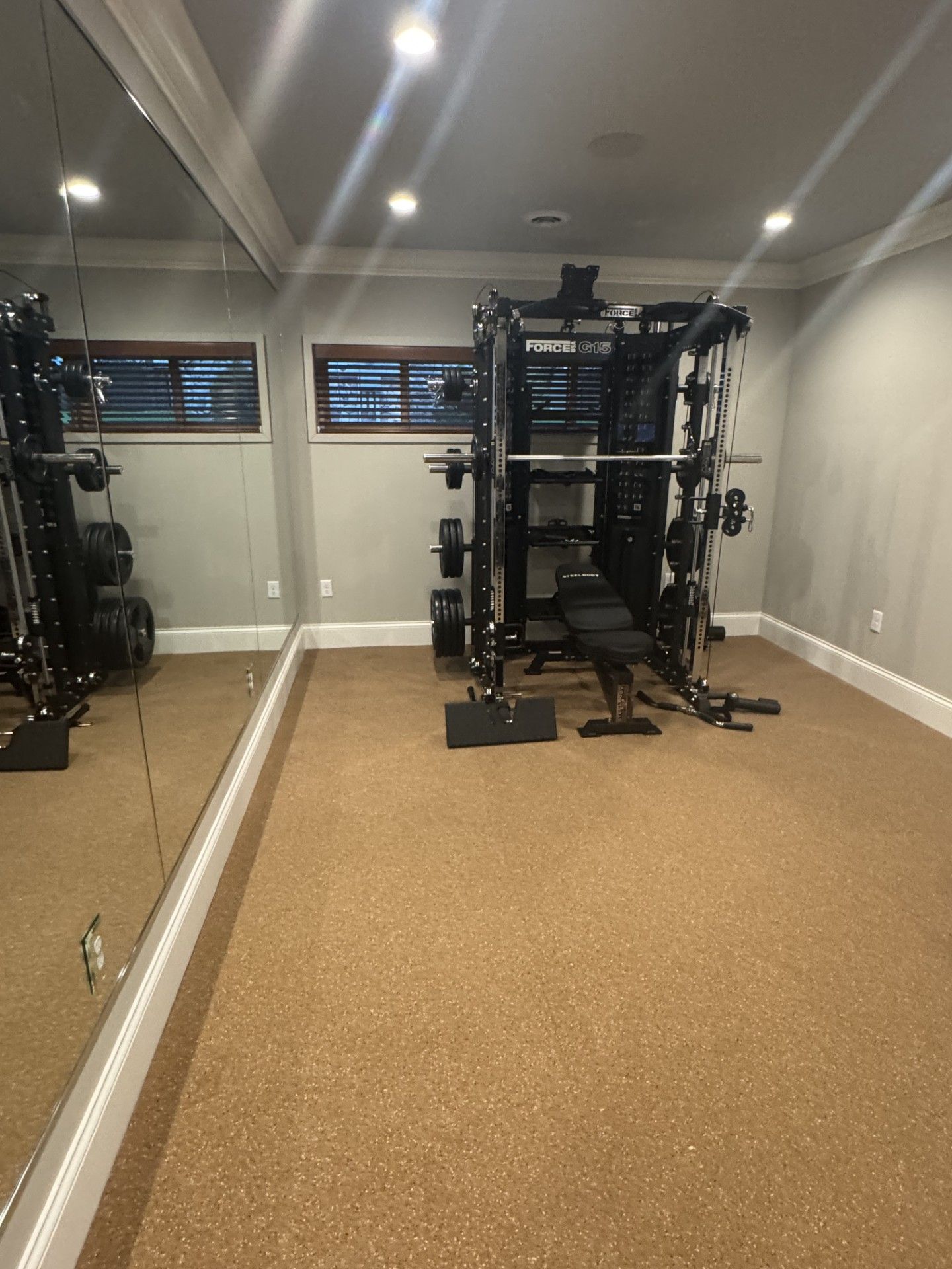 Home gym with weight machine, bench, and mirror on tan floor. Gray walls.