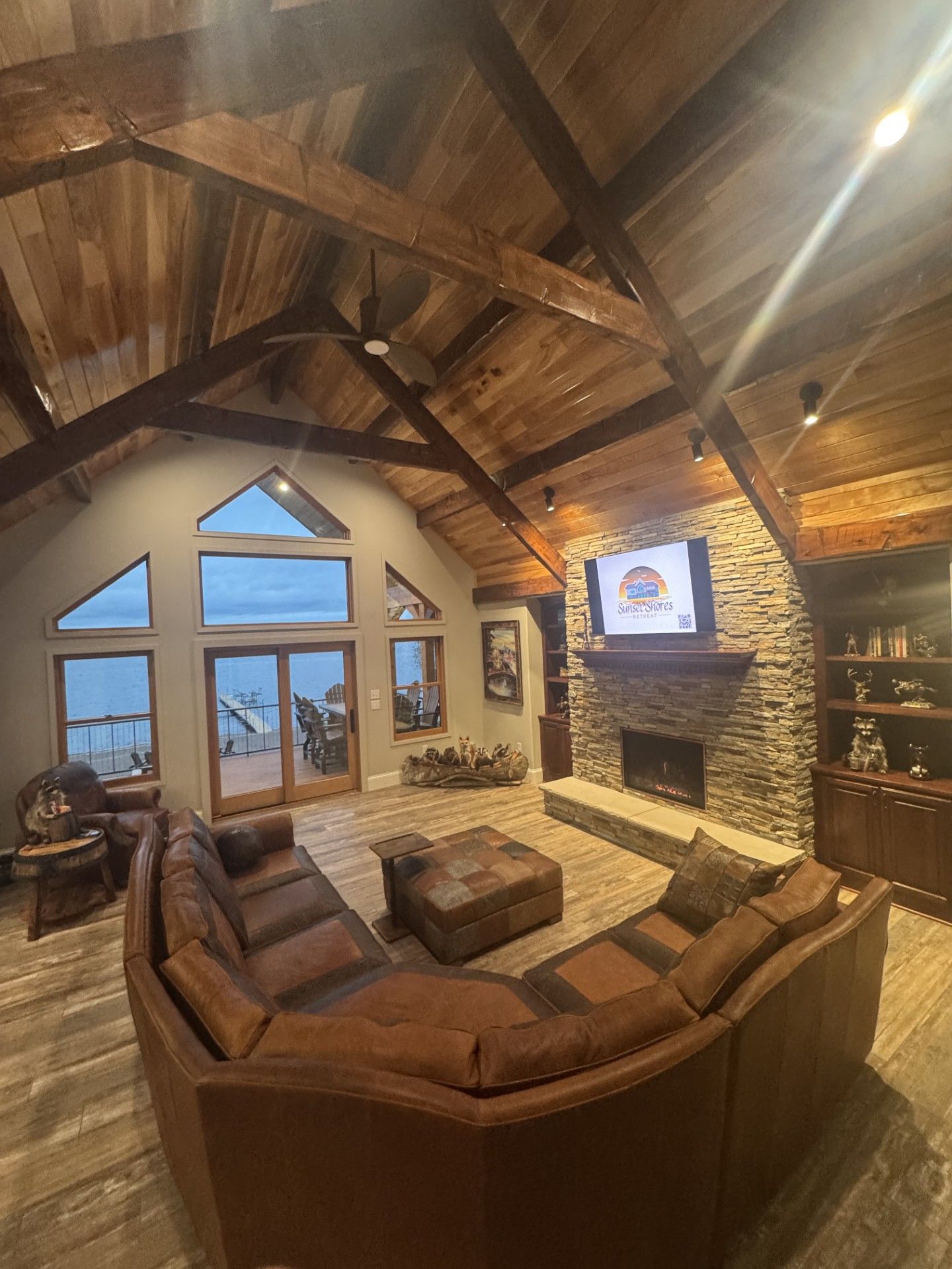 Living room with vaulted wood ceiling, stone fireplace, and brown leather sectional.