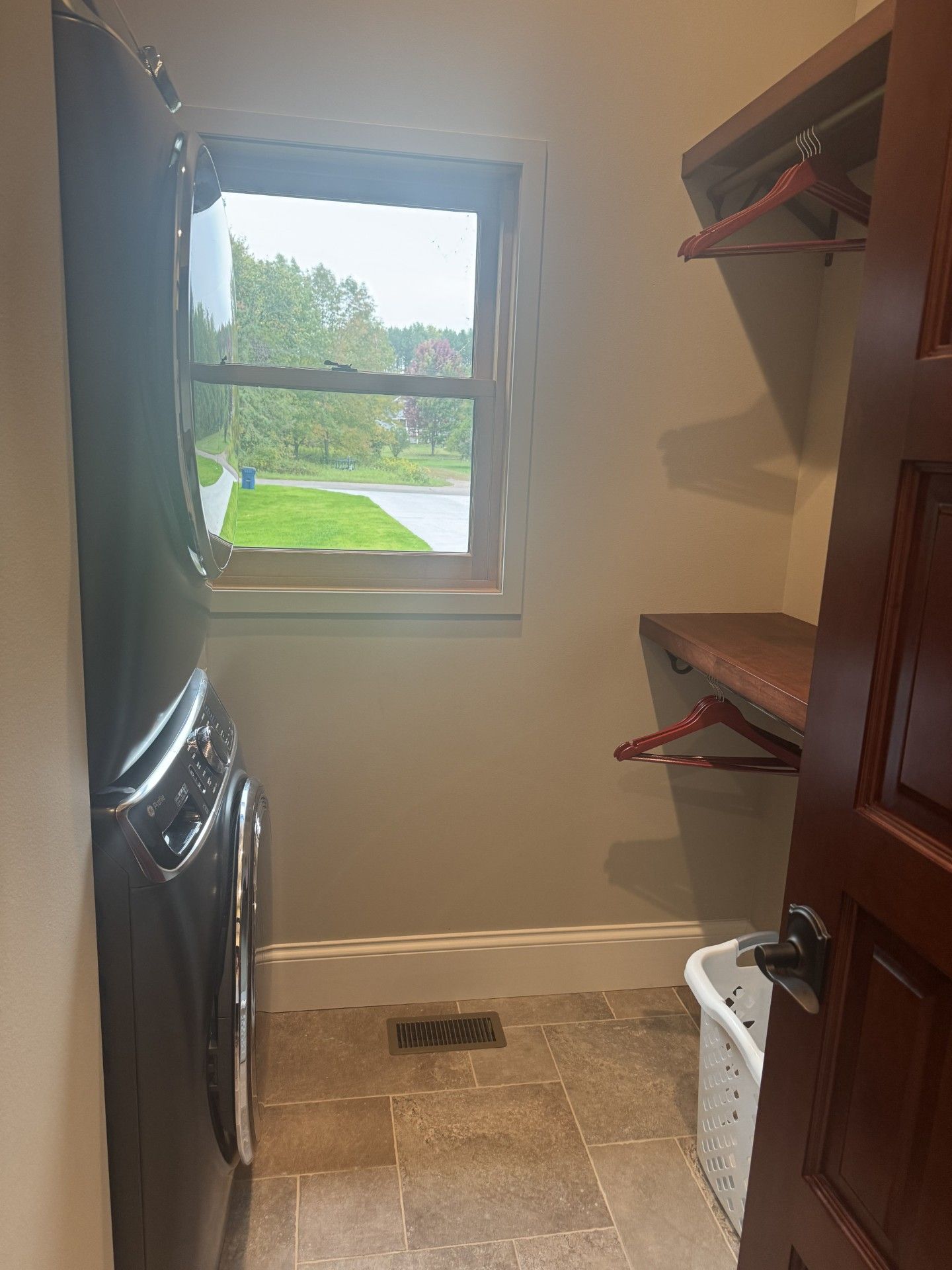 Laundry room with washer, small window, shelf with hangers, and open door.