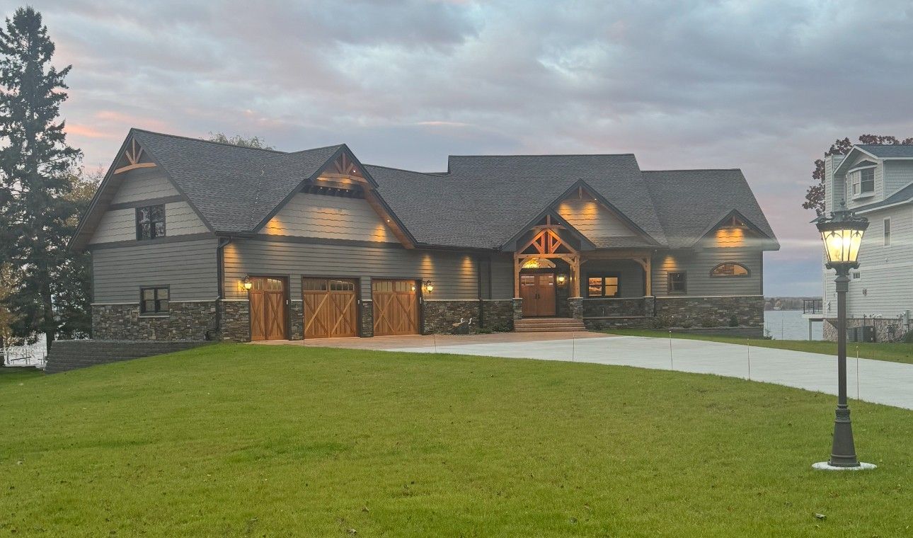 Gray house with stone accents, a gravel driveway, and a lamppost on a grassy lawn at dusk.