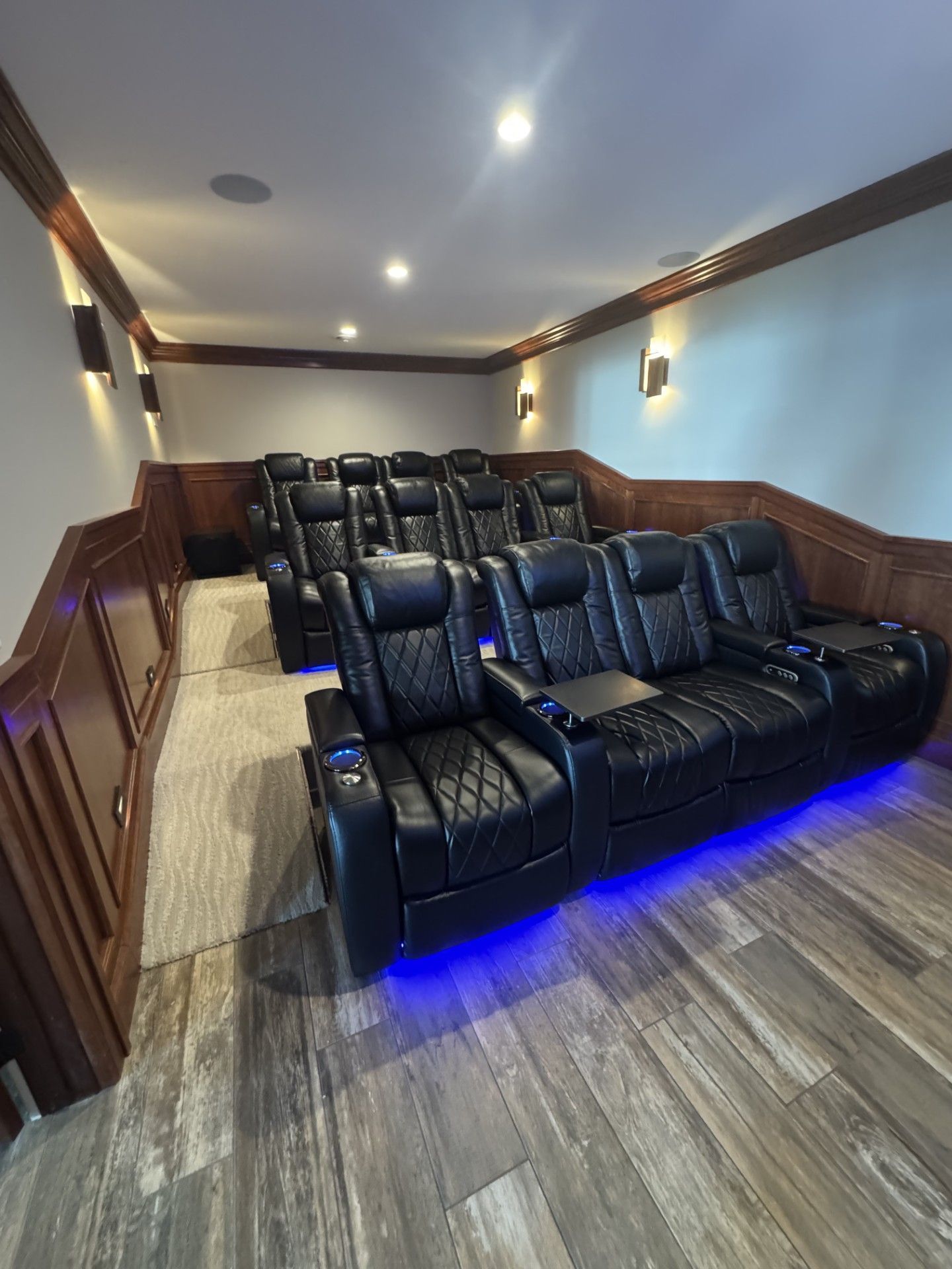 Home theater with tiered seating, black leather recliners, wood paneling, and blue under-seat lighting.