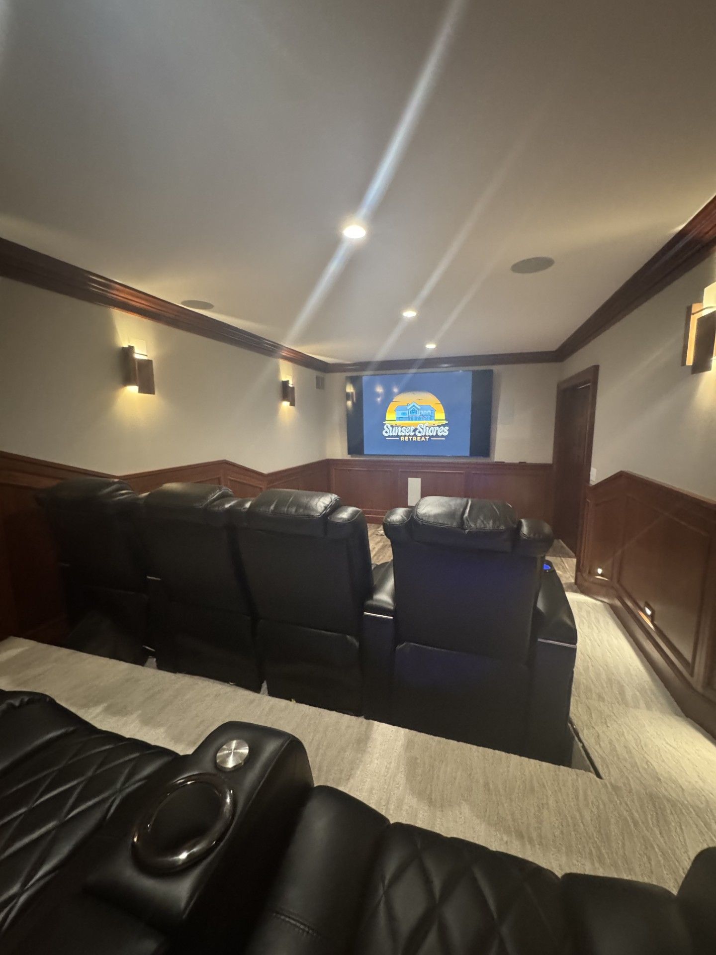 Home theater with black leather recliners, screen, and wood paneling on the walls.