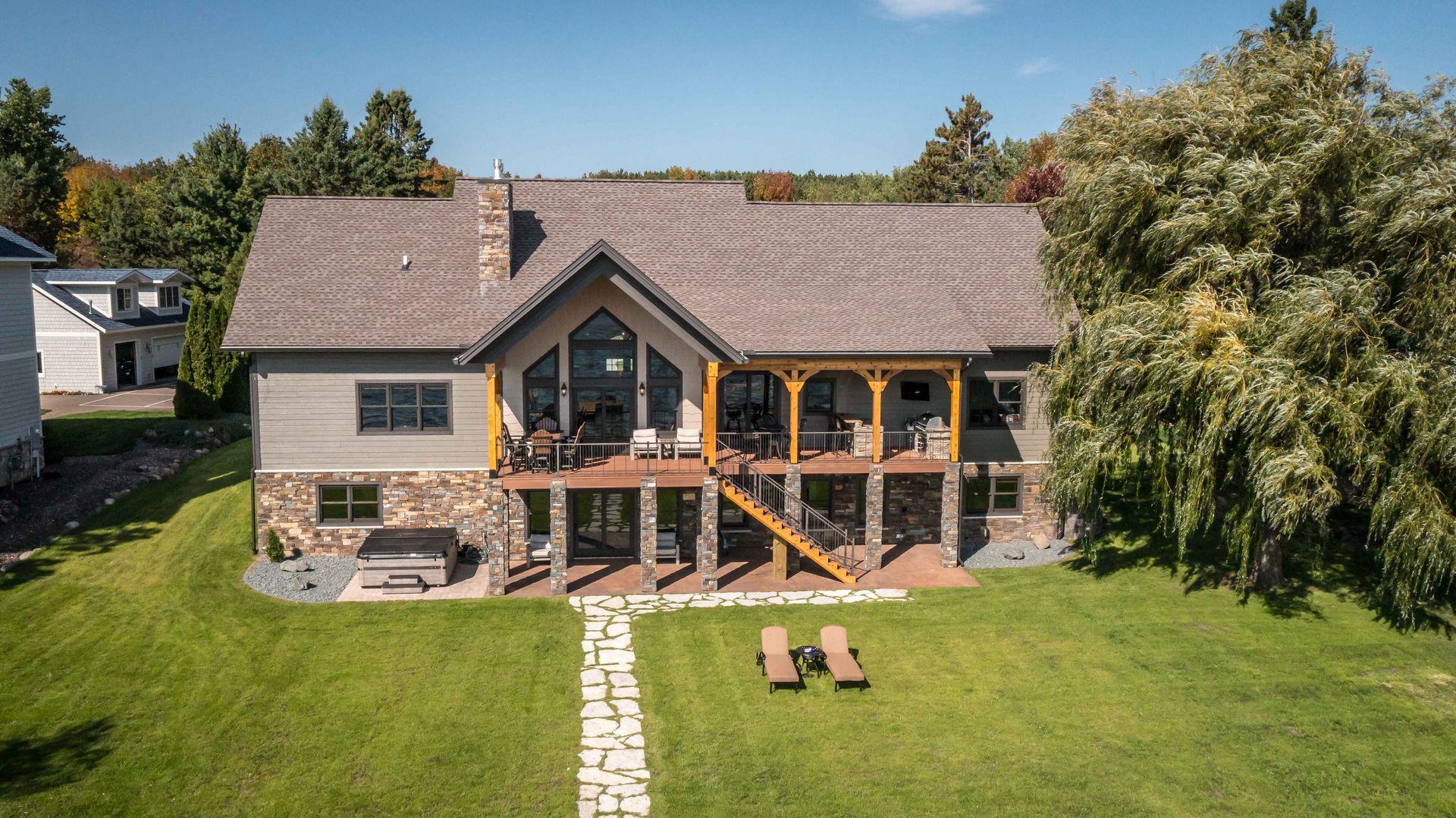 Large house with gray siding, stone accents, and a deck, with a green lawn.