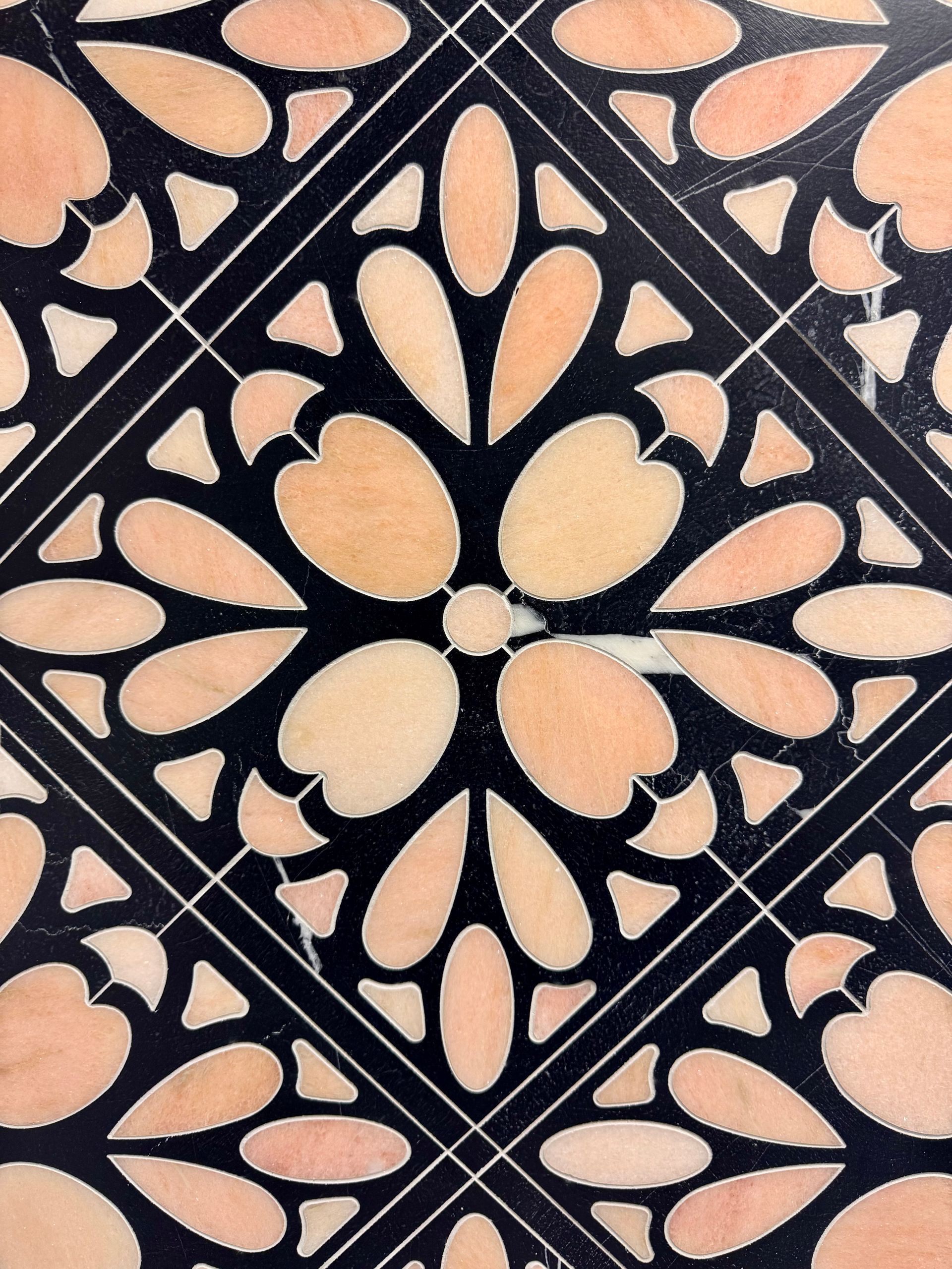 Decorative black tile with peach floral and leaf pattern in a diamond layout