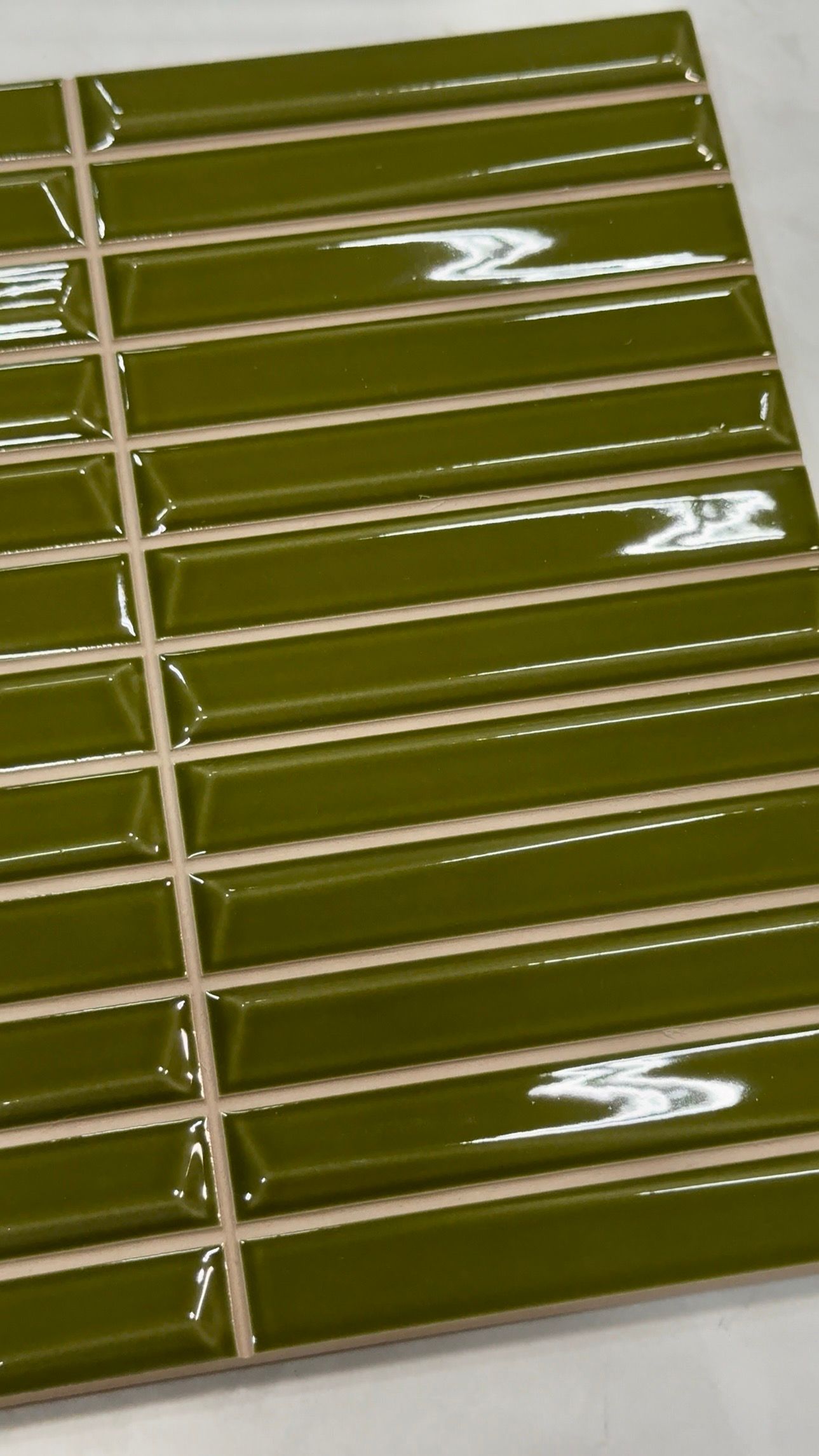 Glossy olive-green tiled surface with white grout lines, viewed at an angle