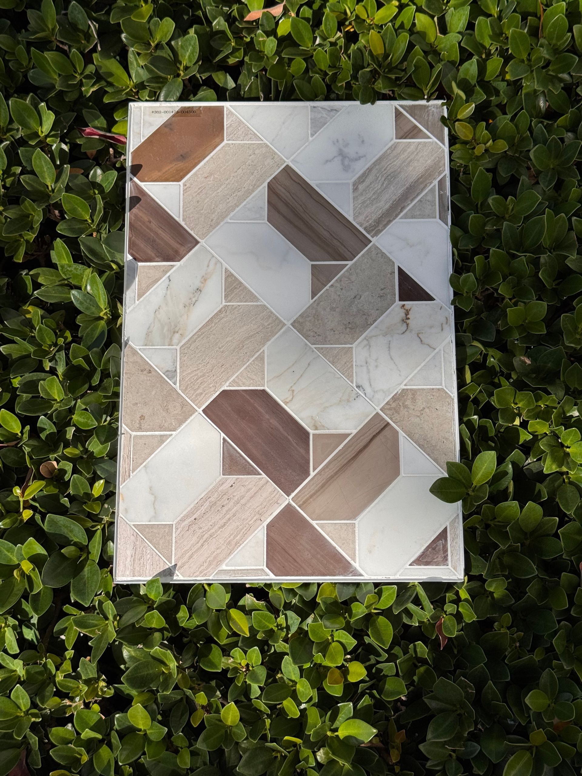 Geometric tile sample in beige, gray, and brown on a leafy green background