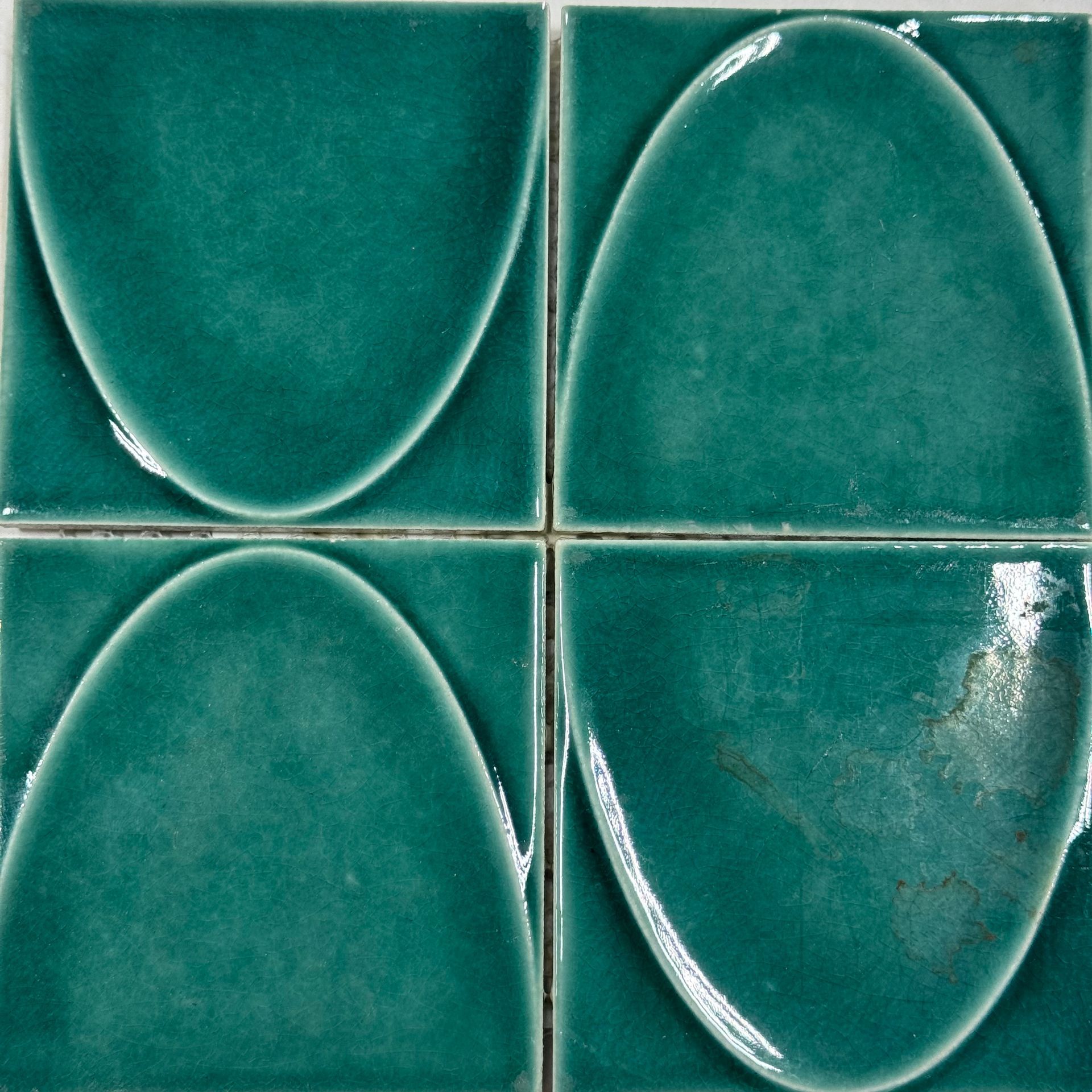 Close-up of four glossy teal ceramic tiles with raised oval shapes arranged in a grid.