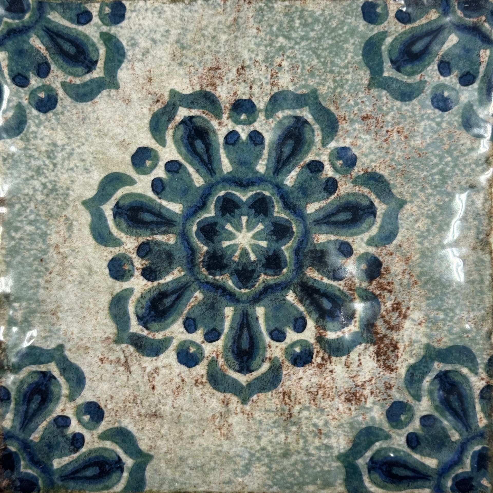 Blue floral ceramic tile with a central rosette pattern and corner motifs on a weathered background