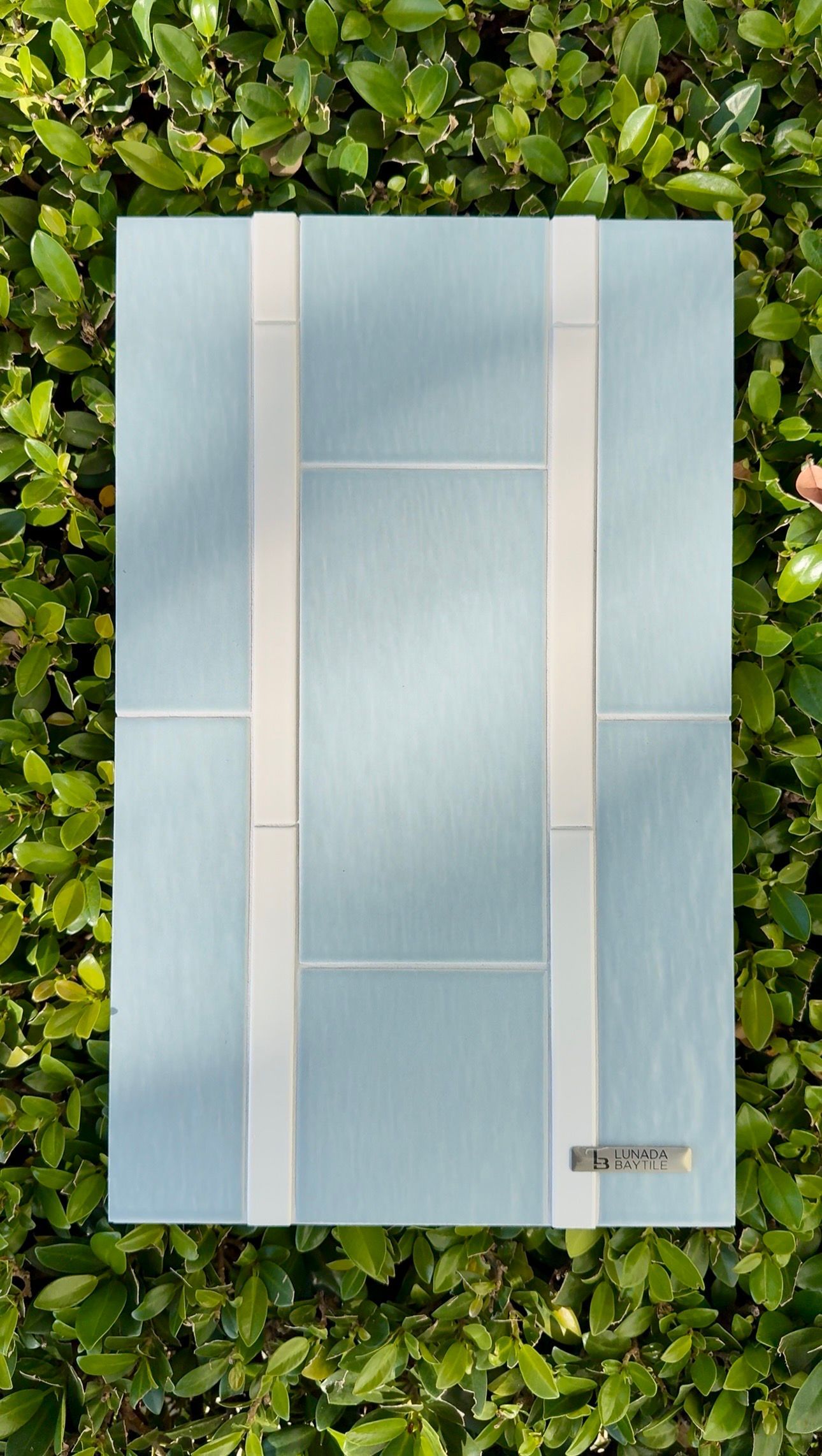 Light blue frosted glass panel with vertical white bands on a leafy green background.
