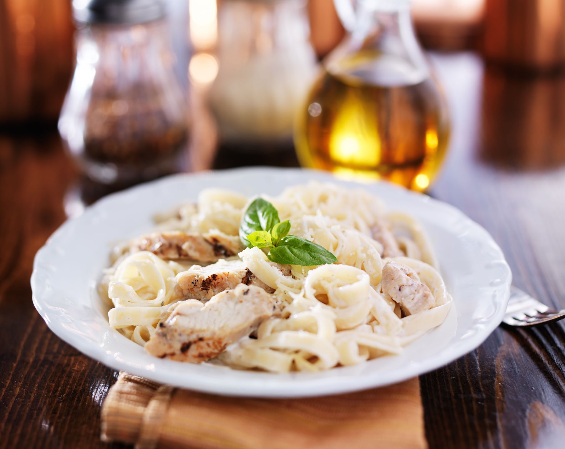 Pasta with chicken and a basil garnish on a white plate; oil and seasonings in the background.