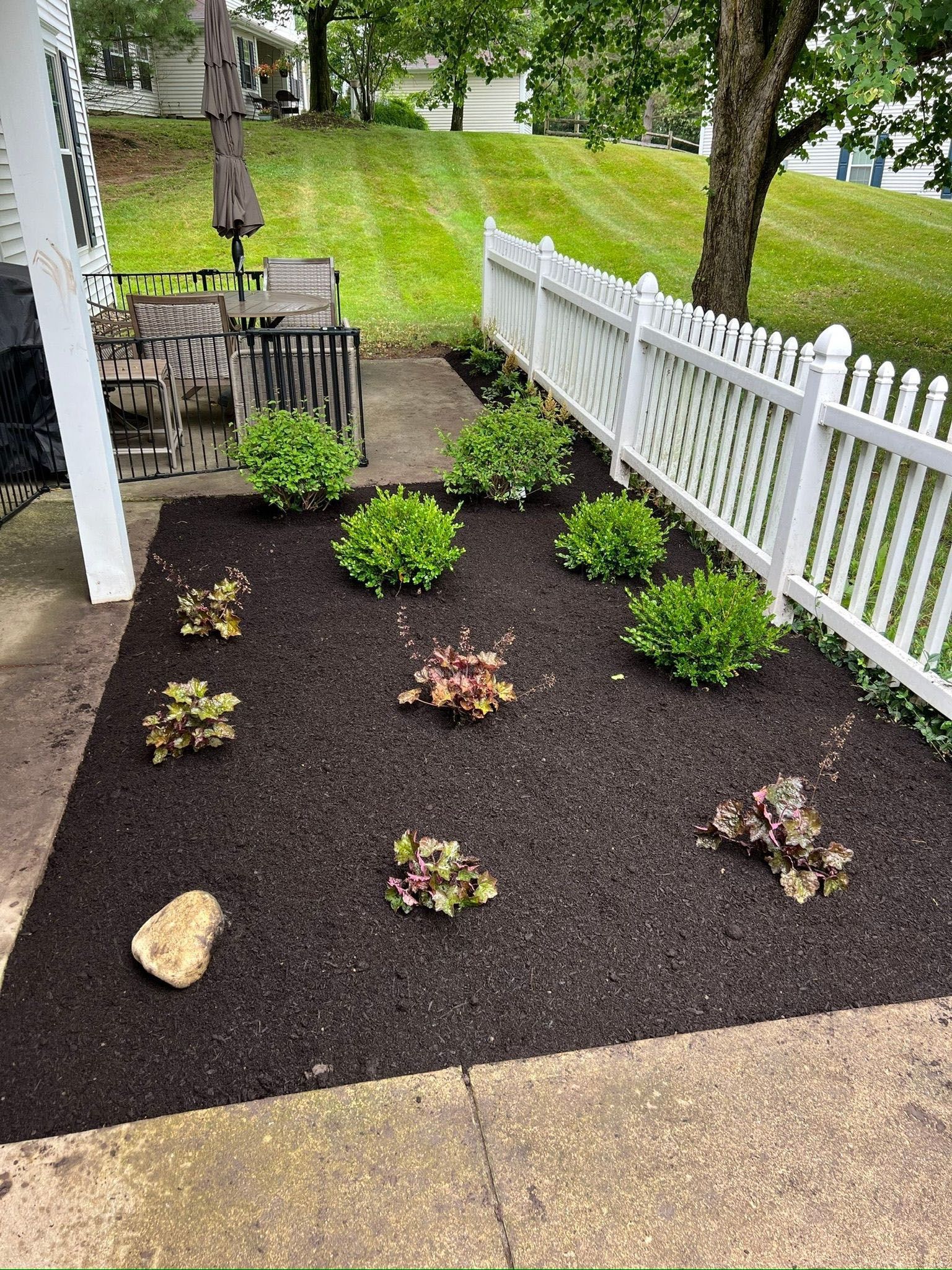 Concrete patio with patio furniture, a brown umbrella, and a dirt patch enclosed by a fence. - After