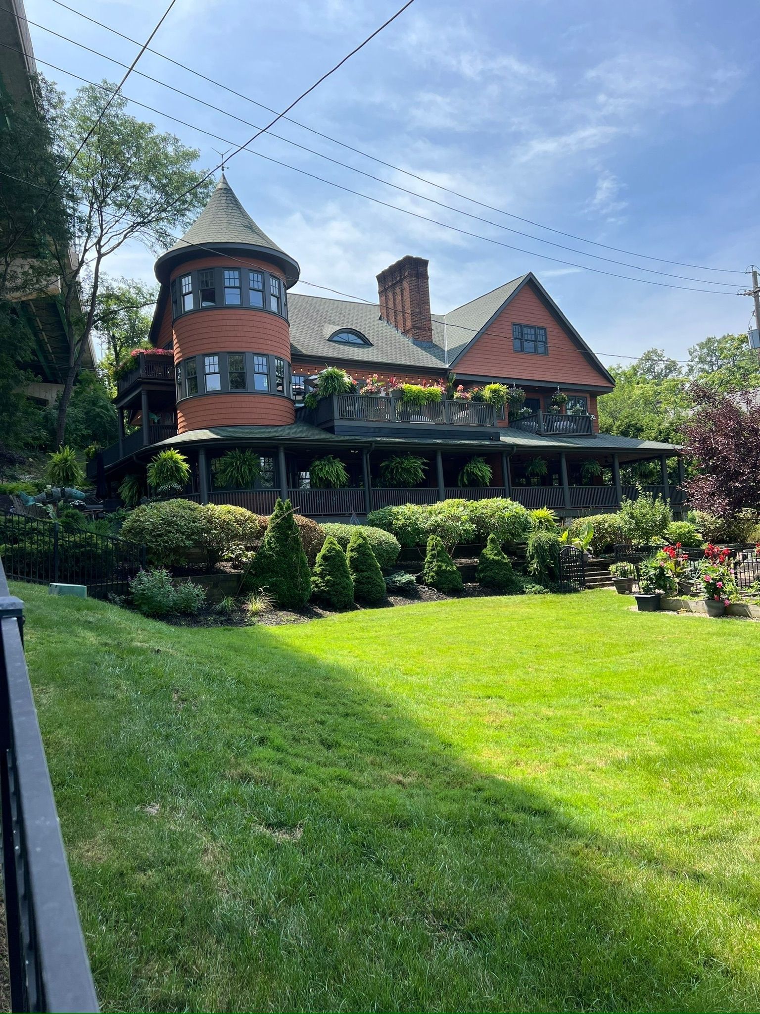 Brick house with a turret, large porch, and green lawn on a sunny day.