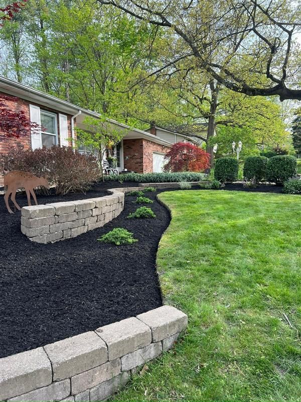 Landscaped yard with black mulch, retaining wall, green grass, and house.