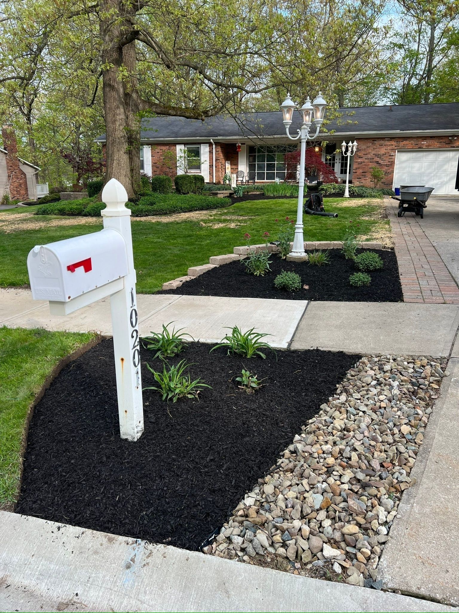 White mailbox with red flag in front yard with black mulch and a brick house in the background.