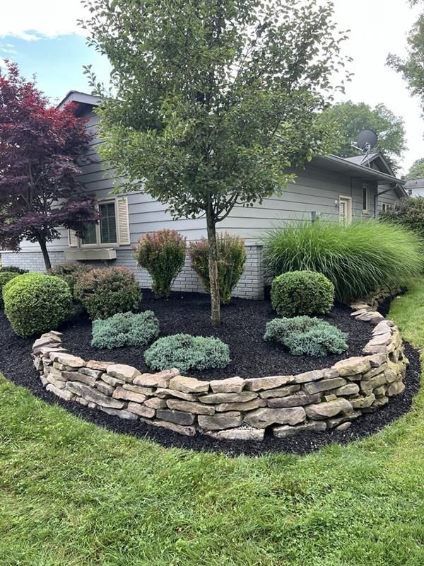 A stone wall surrounds a tree in a garden in front of a house.