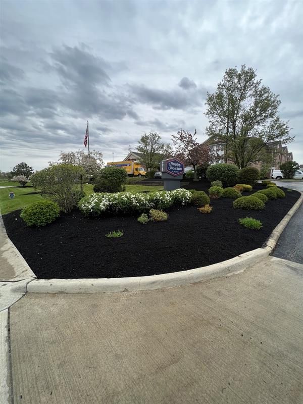 A circular garden with black mulch and flowers in front of a building.